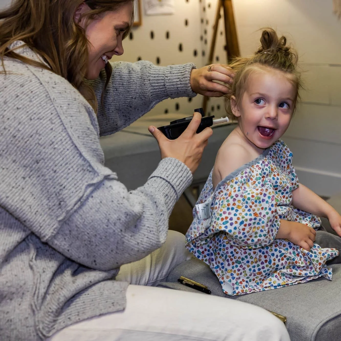 Dr. Jordan Fennelly of Two Sparrows Chiropractic in Whitefish, MT is using a nervoscope to examine a young girl's spine, who is sitting on a couch with a dressing gown on, smiling and looking happy.
