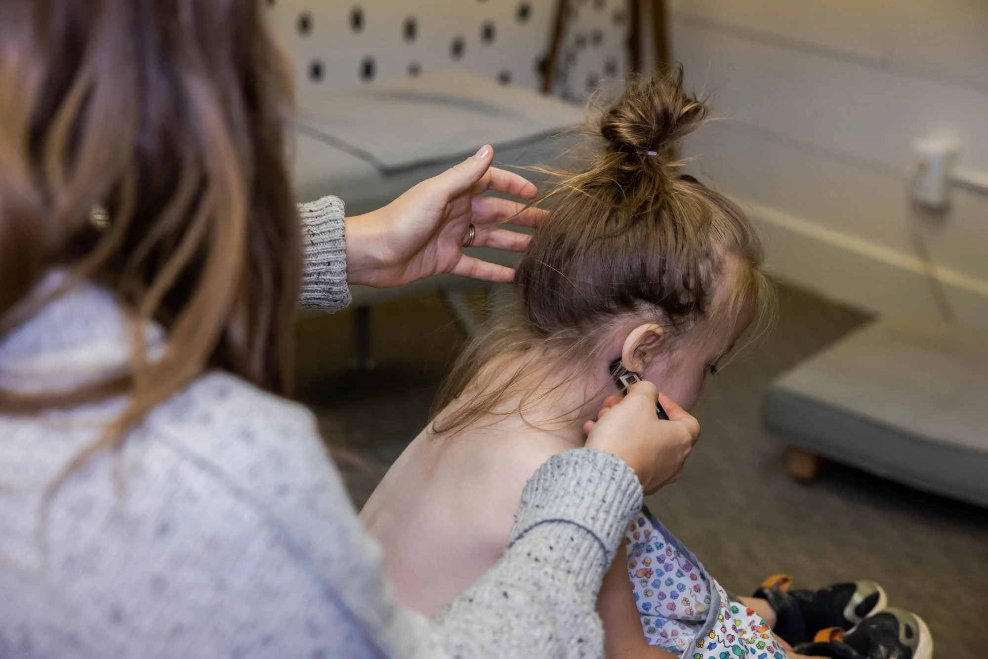 Dr. Jordan Fennelly of Two Sparrows Chiropractic in Whitefish, MT is using a nervoscope to examine a young girl's spine, who is sitting on a couch with a dressing gown on, smiling and looking happy.