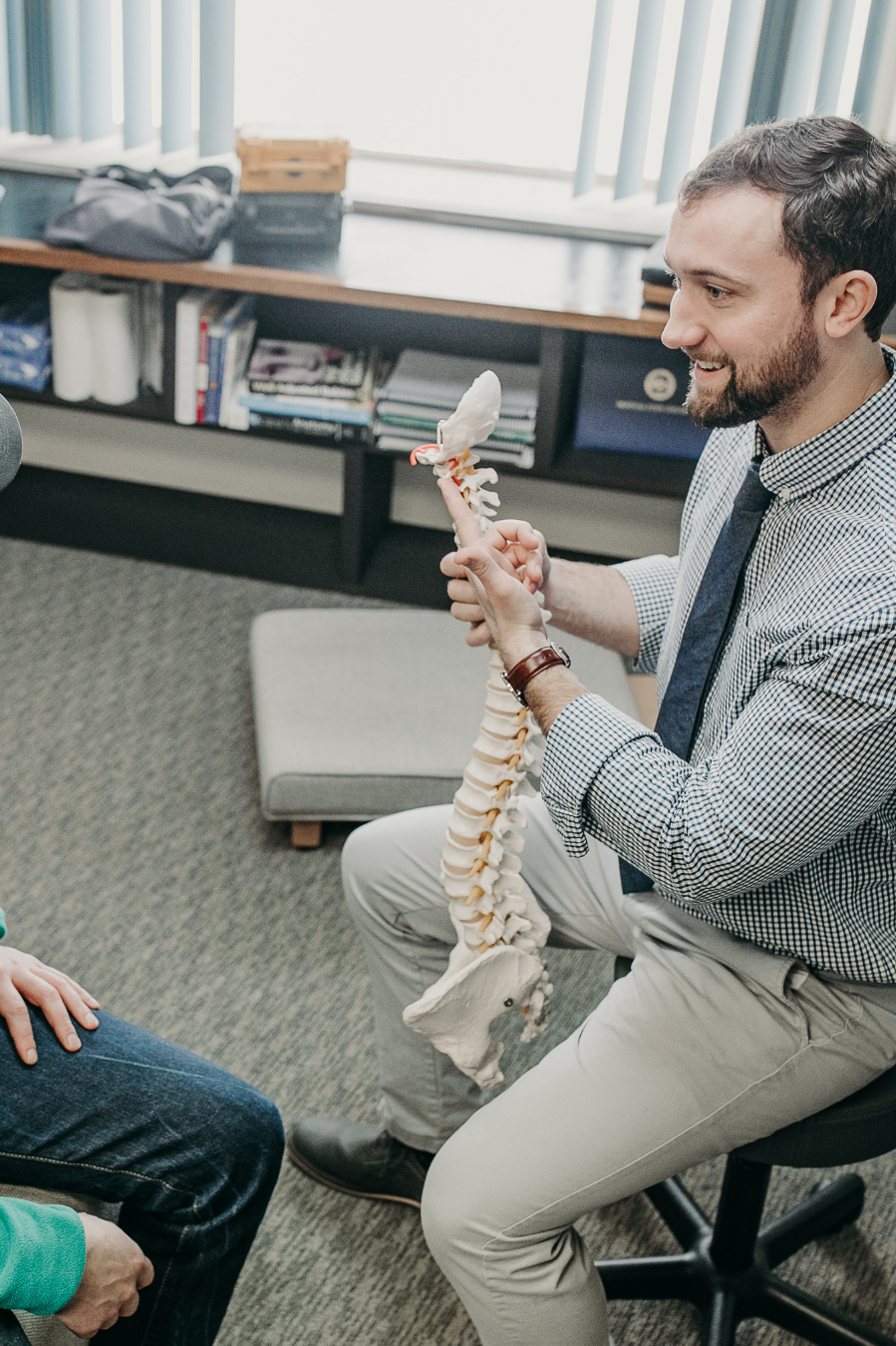 Dr. Peter Fennelly of Two Sparrows Family Chiropractic in Whitefish, Montana holding a model of a human spine during a chiropractic report of findings with a patient, educating on the benefits of chiropractic care.