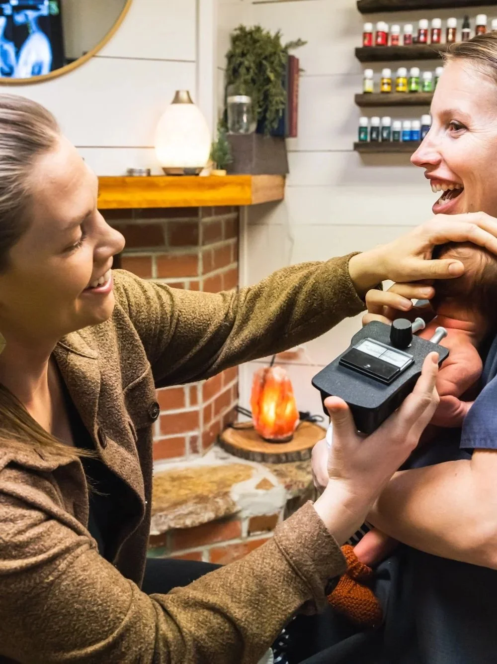 Dr. Jordan Fennelly of Two Sparrows Family Chiropractic in Whitefish, Montana is in her office with a mom and baby, and she is using a temperature tracking tool on the baby's neck to see if there are temperature changes in the baby's spine.