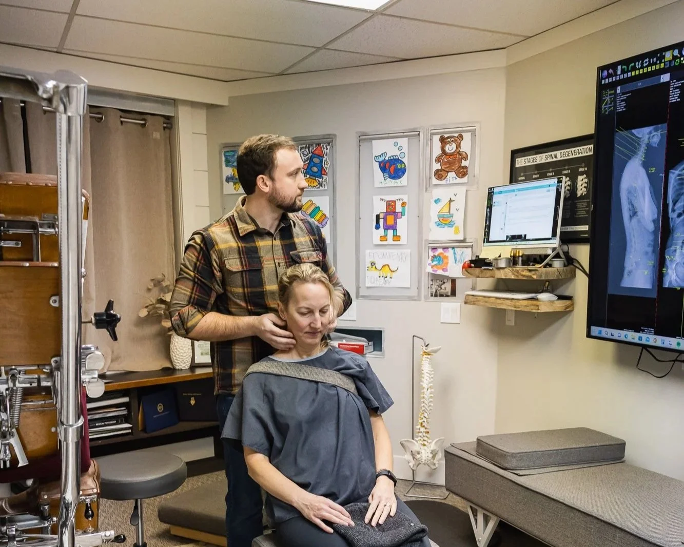 Dr. Peter Fennelly of Two Sparrows Chiropractic in Whitefish, MT is using a nervoscope to examine a young woman's spine, who is sitting on a chair with a dressing gown on, smiling and looking happy.