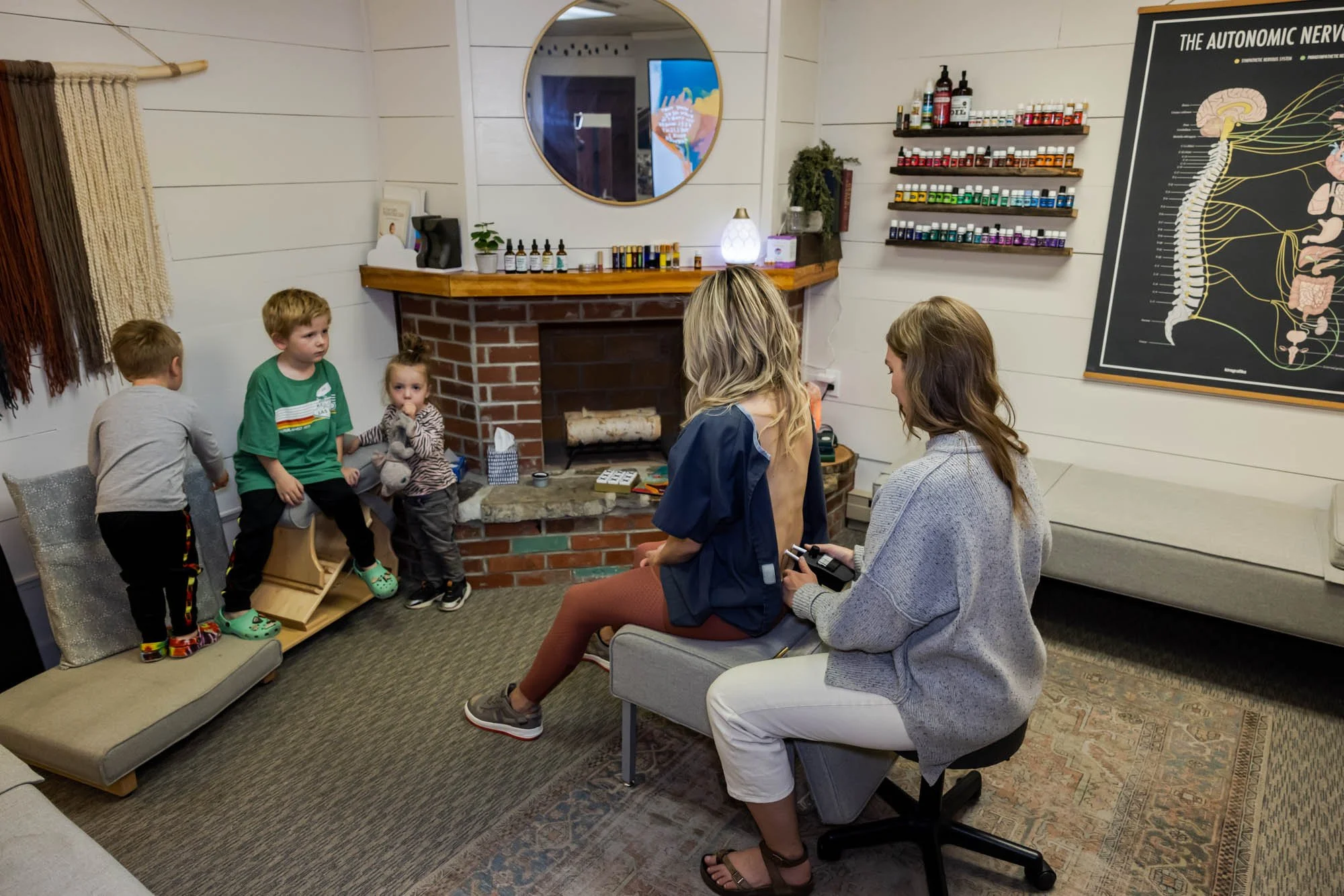 Dr. Jordan Fennelly of Two Sparrows Family Chiropractic in Whitefish, Montana doing a chiropractic analysis on a mom, while her kids play in the background.