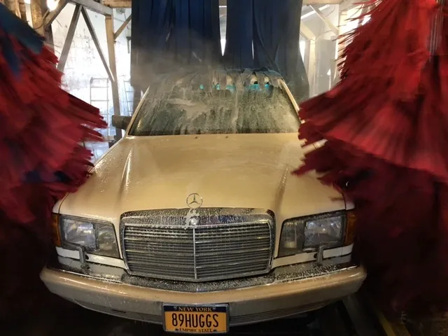 A vintage white Mercedes-Benz car in a car wash with large red brushes on either side.