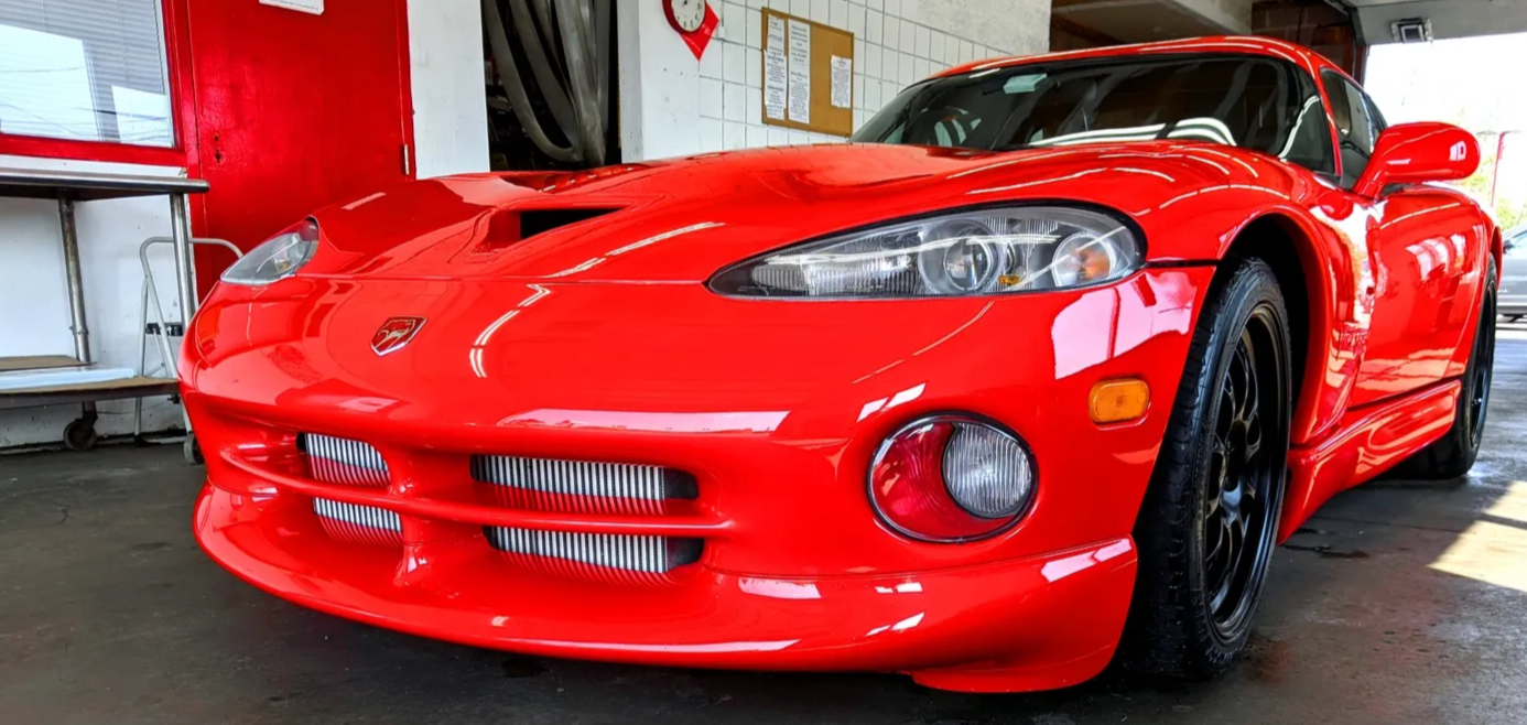 Red sports car parked indoors, front view showing sleek design, round headlights, and mesh grille.
