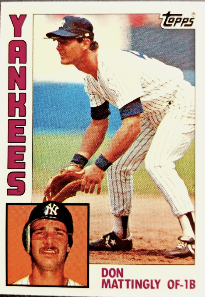 Baseball card featuring Yanks player Don Mattingly, wearing a batting helmet, standing on a field, with a small inset photo of him with a helmet on and a serious expression. The card has the Topps logo at the top right, and the text 'YANKESS' on the left side in bold pink letters, and 'DON MATTINGLY OF-1B' at the bottom in pink.