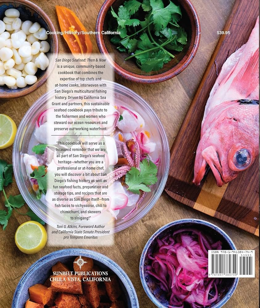 Assorted seafood ingredients including fish, octopus, and clams, along with vegetables such as cilantro, pickled onions, and limes, displayed on a wooden surface.
