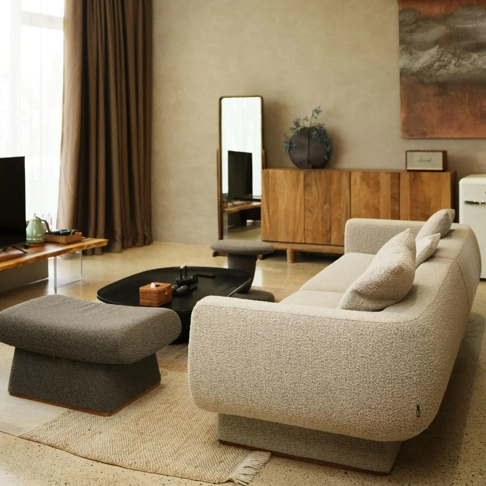 Living room with a beige sofa, a black coffee table, a matching ottoman, a wooden sideboard, a mirror, a TV, and curtains near a window.