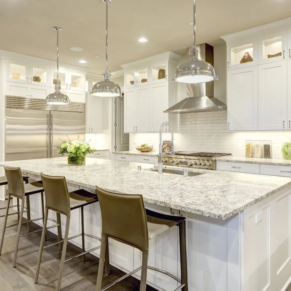Modern kitchen with white cabinetry, stainless steel appliances, granite island, and three pendant lights.