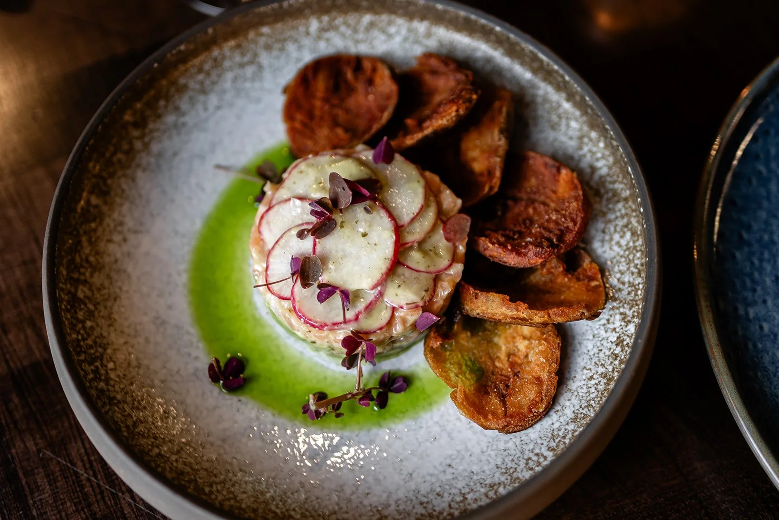 A plated dish with sliced radishes, microgreens, green sauce, and roasted potato wedges.