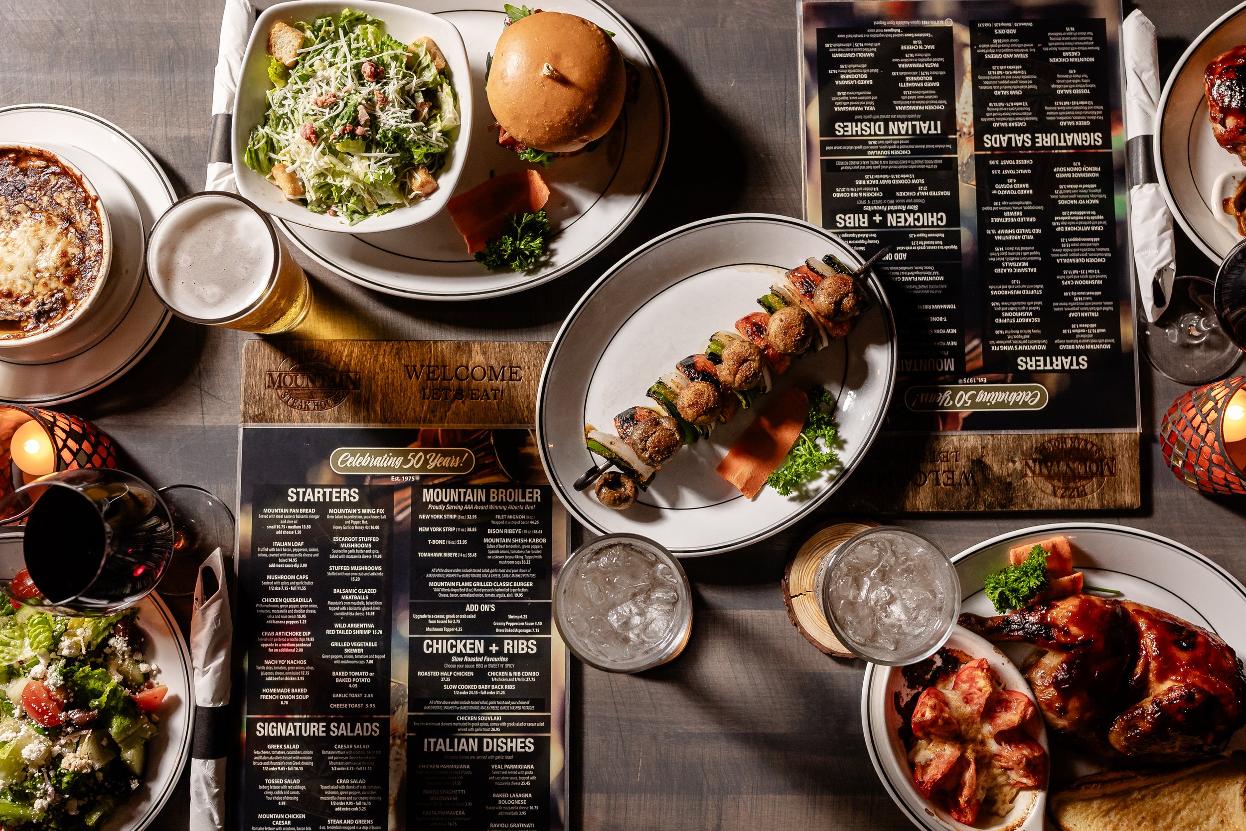 A top-down view of a table with various dishes including salads, a burger, skewers, pizza, drinks, and a menu.