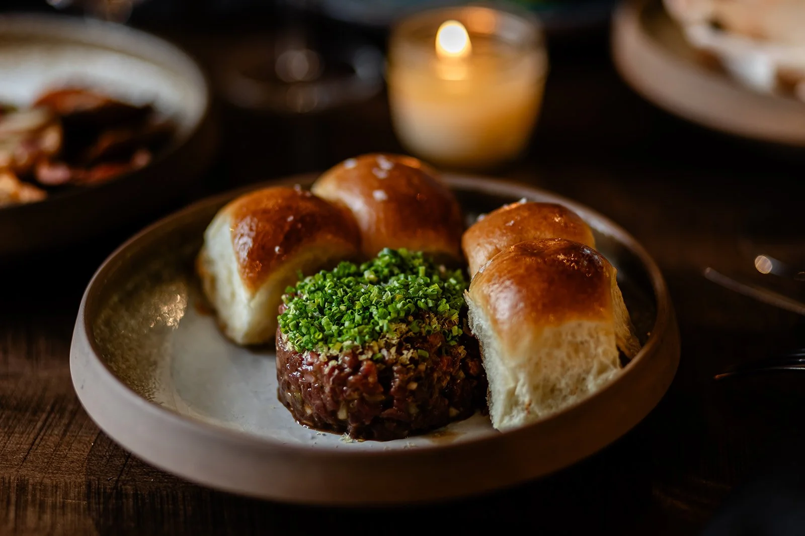 Dish featuring five dinner rolls with shiny, golden-brown crust, one with chopped chives on top, served on a textured, metallic plate.