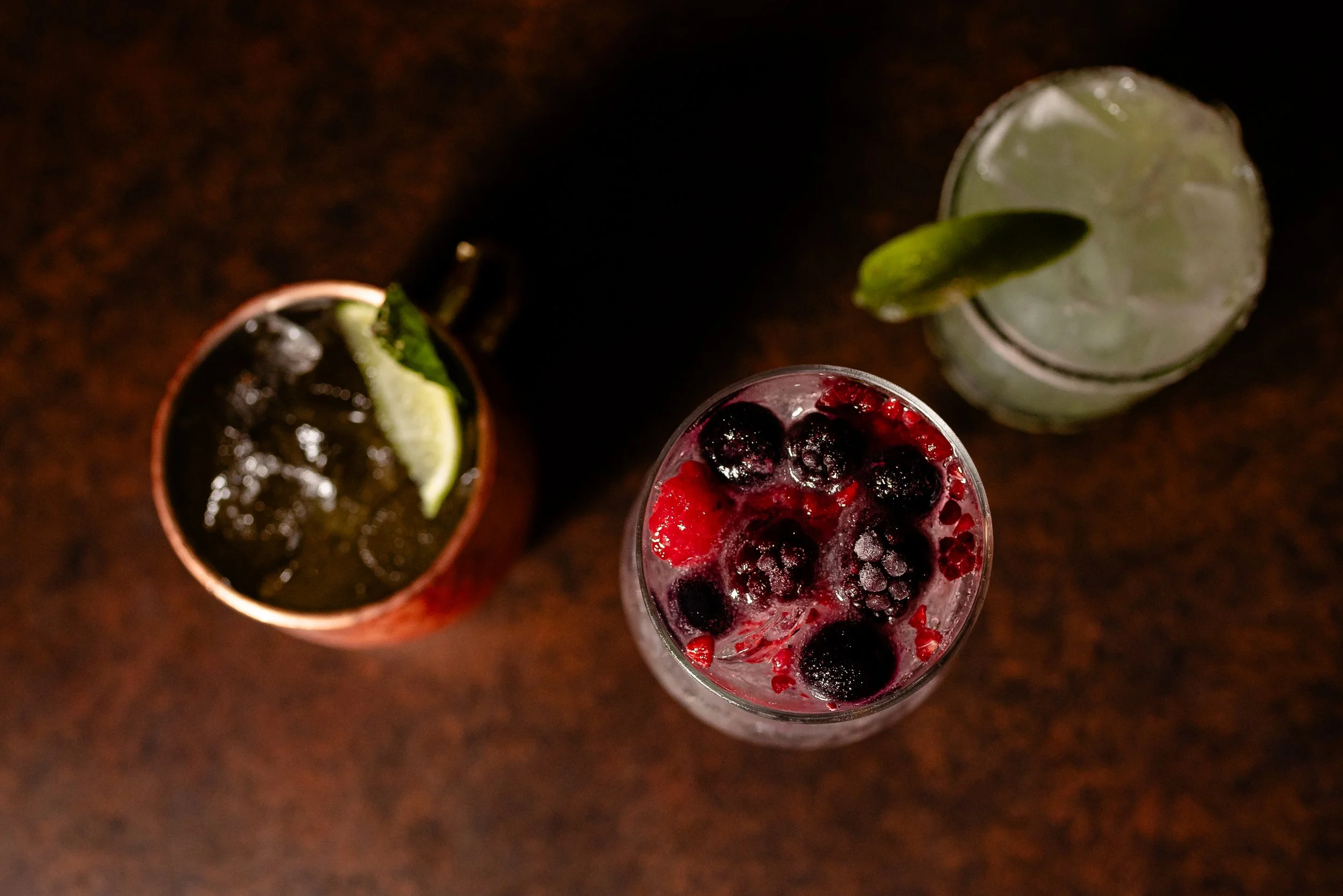 Three drinks viewed from above, each garnished with fruit slices and berries.