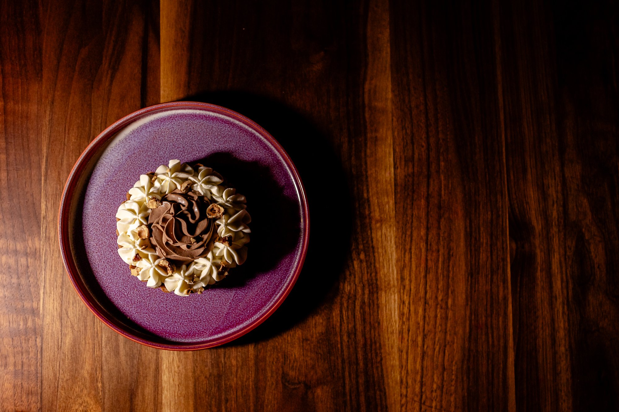 A bowl of dessert with whipped cream and chocolate toppings on a wooden table.