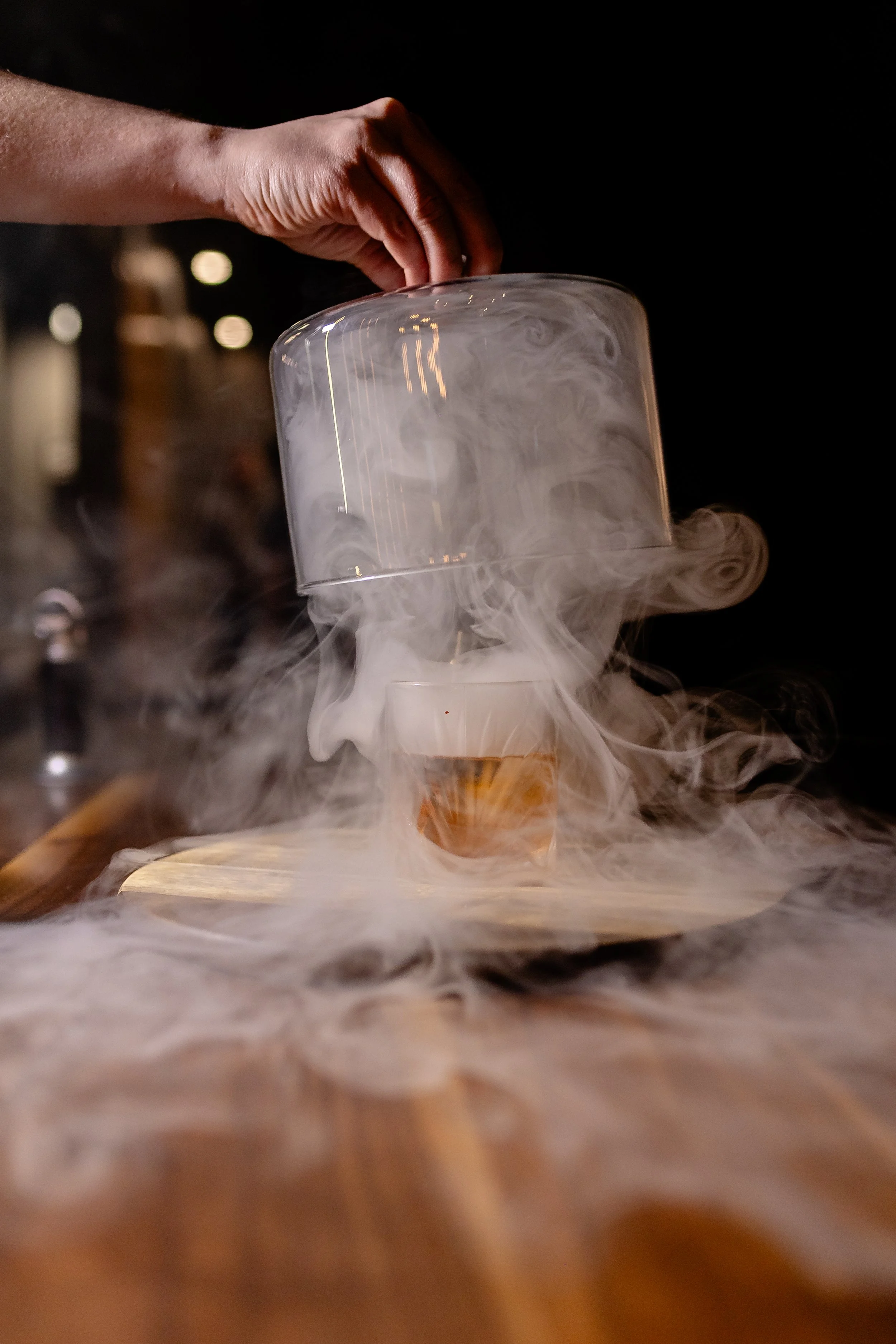 A hand releasing a glass with dry ice inside, creating white smoke around it.