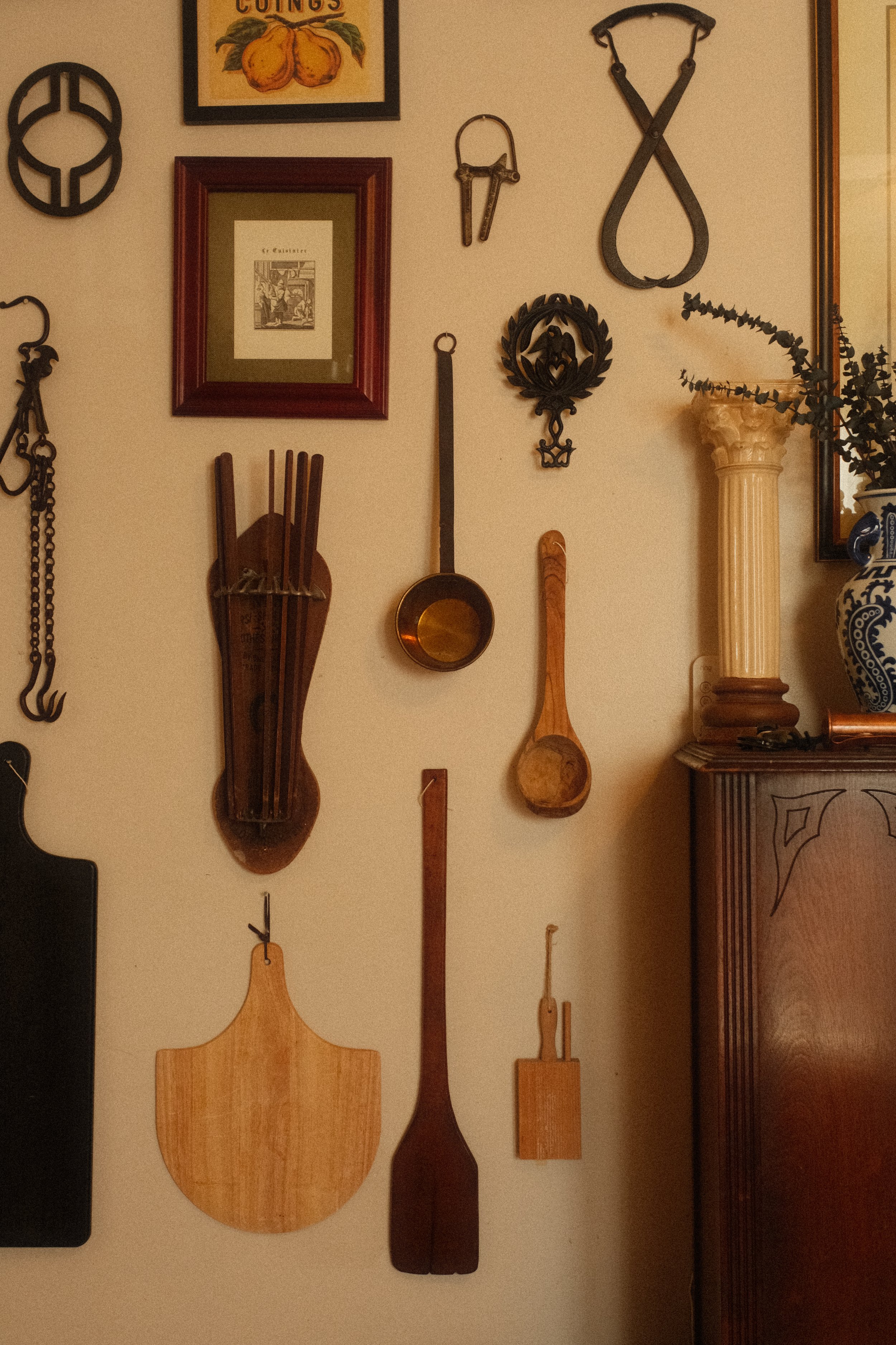 A wall decorated with various vintage kitchen tools and artwork, including wooden cutting boards, a ladle, and a framed print.