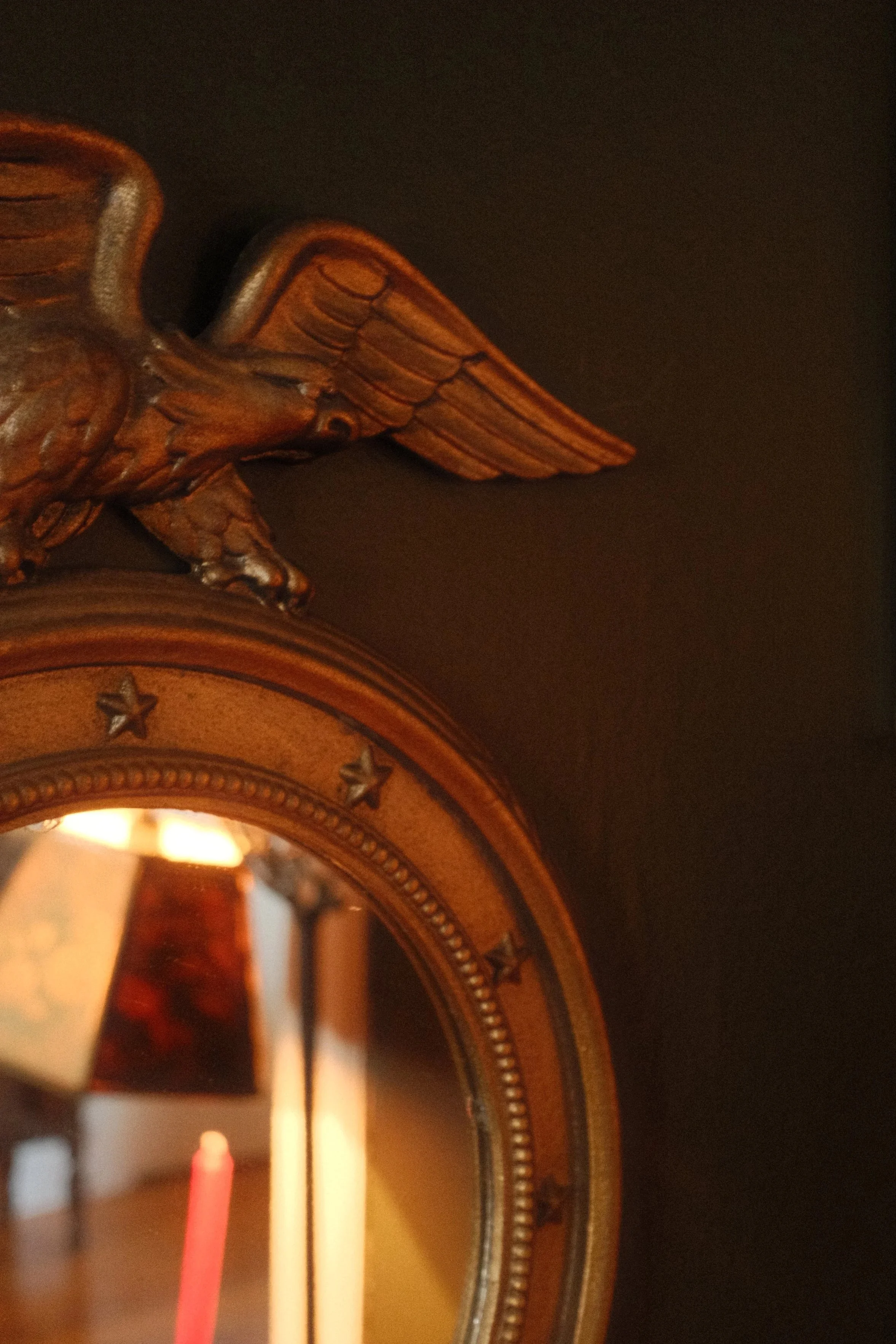 Close-up of a wooden eagle wall clock with ornate details and a mirror in the background.