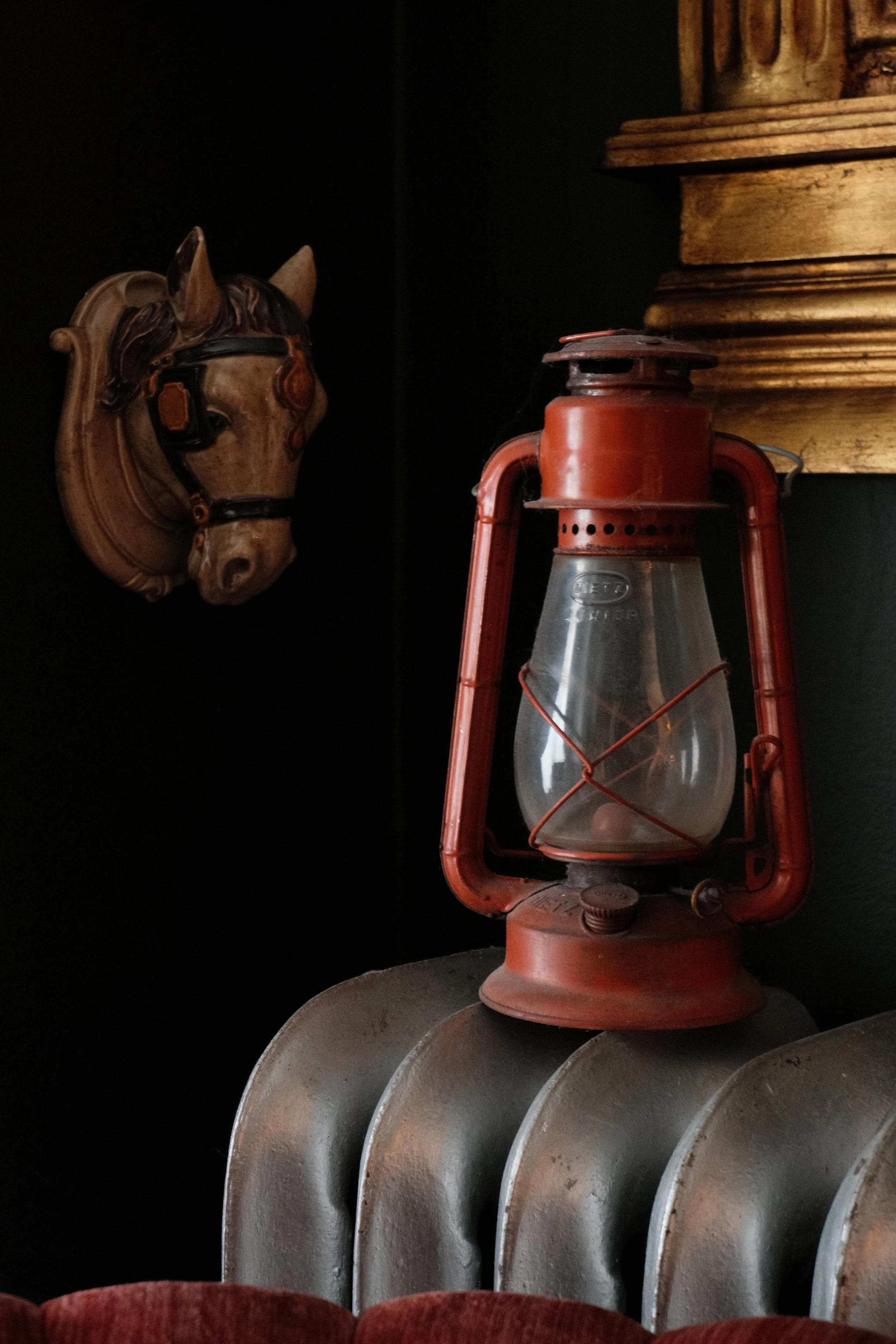 Decorative horse head wall sculpture, vintage red lantern, and a set of metallic round trays or plates.