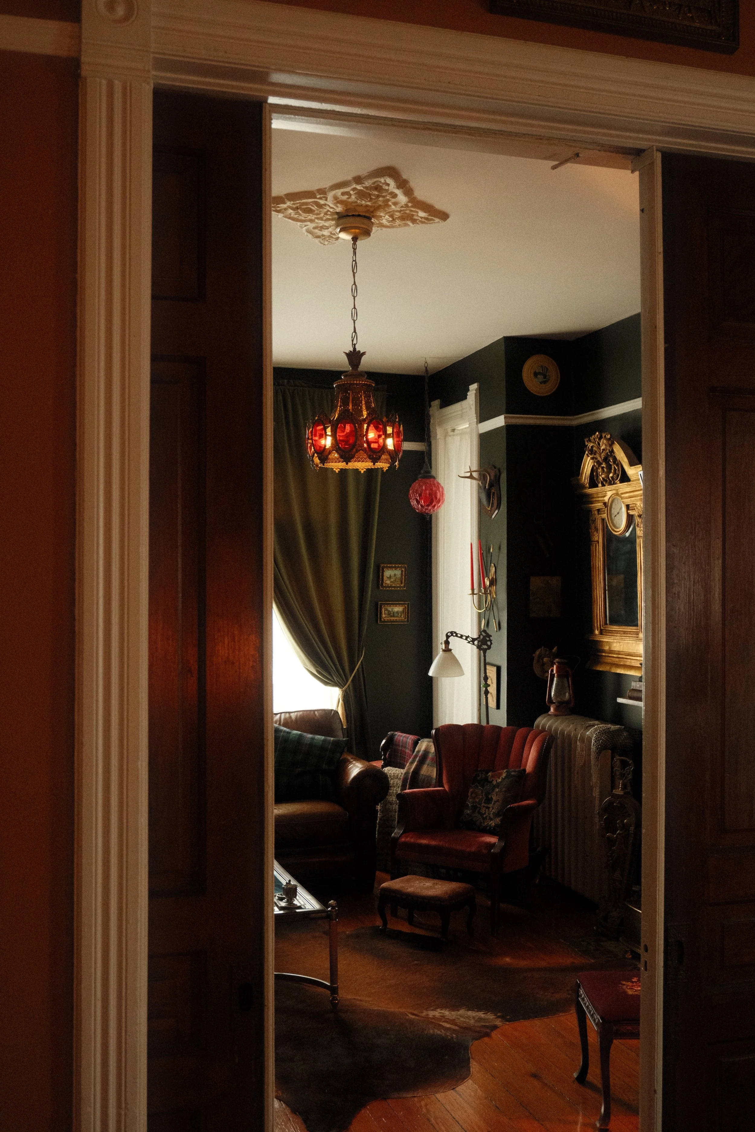 A room reflected in a mirror with vintage furniture, a chandelier, and dark walls, decorated in an antique style.