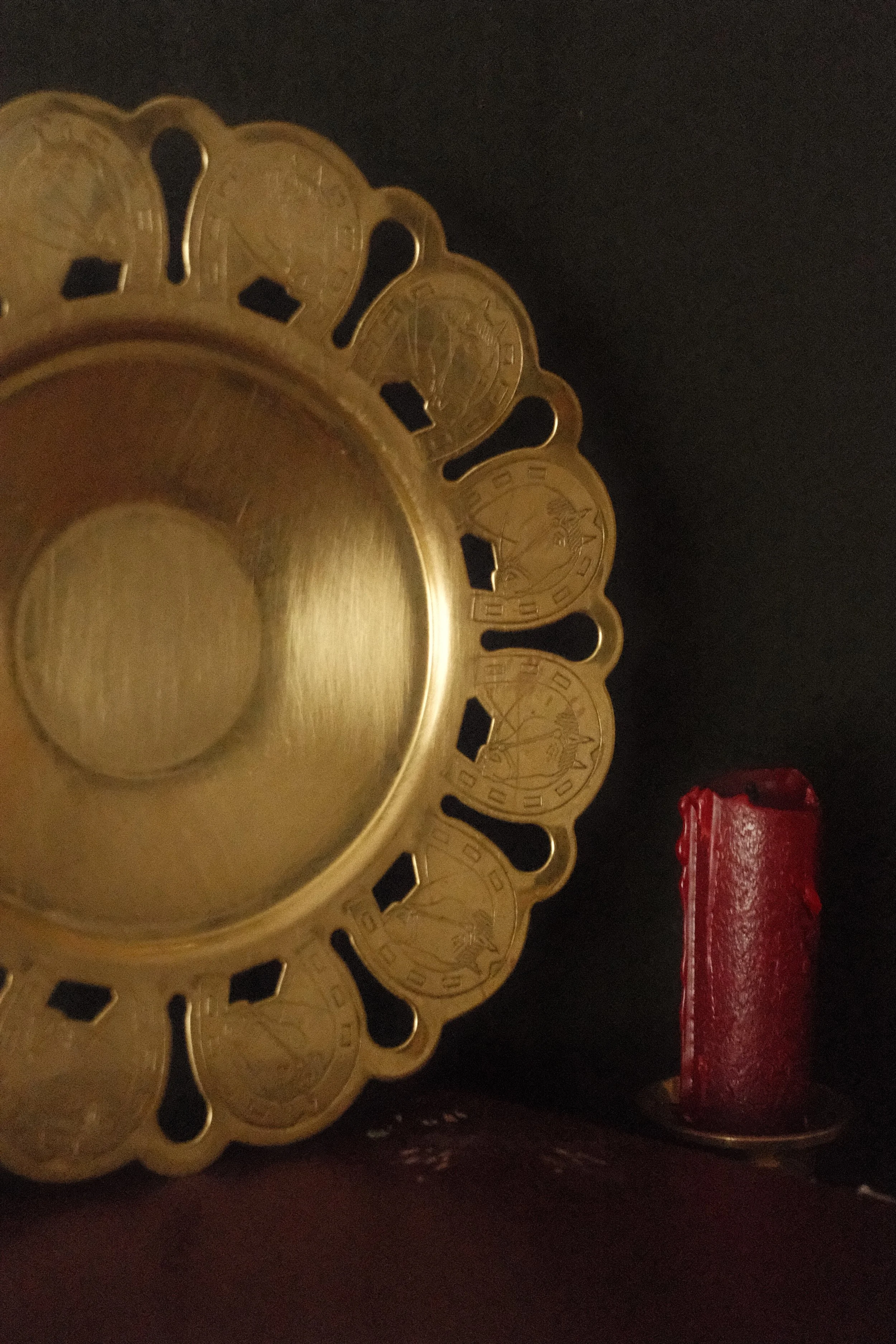 Close-up of a gold rimmed plate with a decorative edge holding several coins, with a red object partially visible behind it.