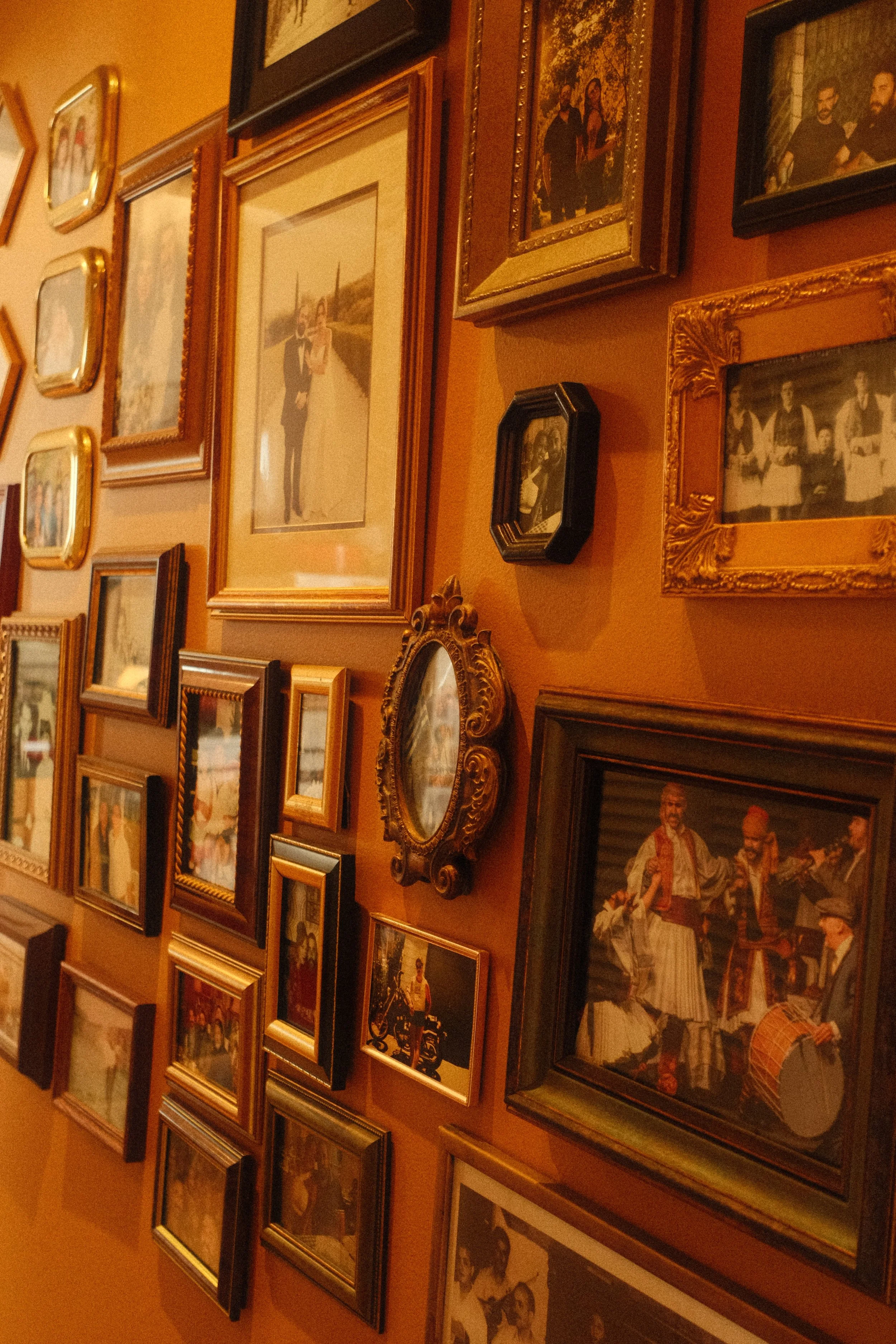 Wall decorated with various framed photographs, including a large wedding photo of a couple, and other black and color images in ornate and simple frames, arranged in a gallery style.