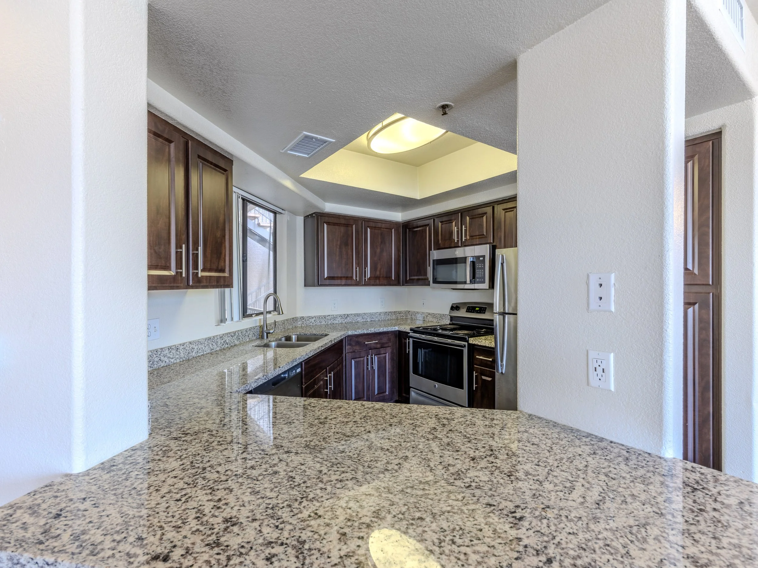 Kitchen with dark wood cabinets, stainless steel appliances, granite countertops, and a ceiling light fixture.