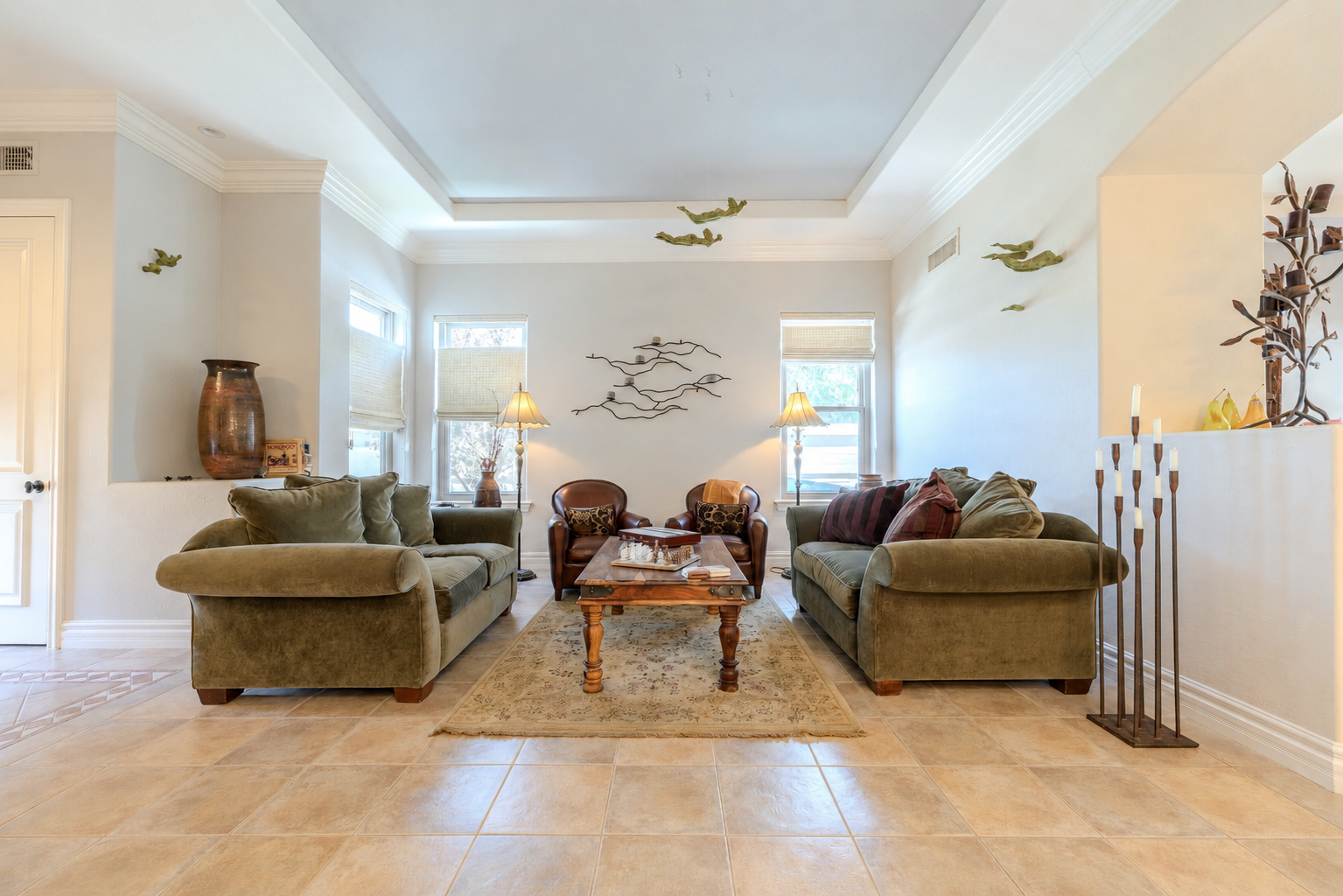 Living room with two green sofas, a wooden coffee table, and two leather armchairs, with decorative plants, lamps, and wall art.