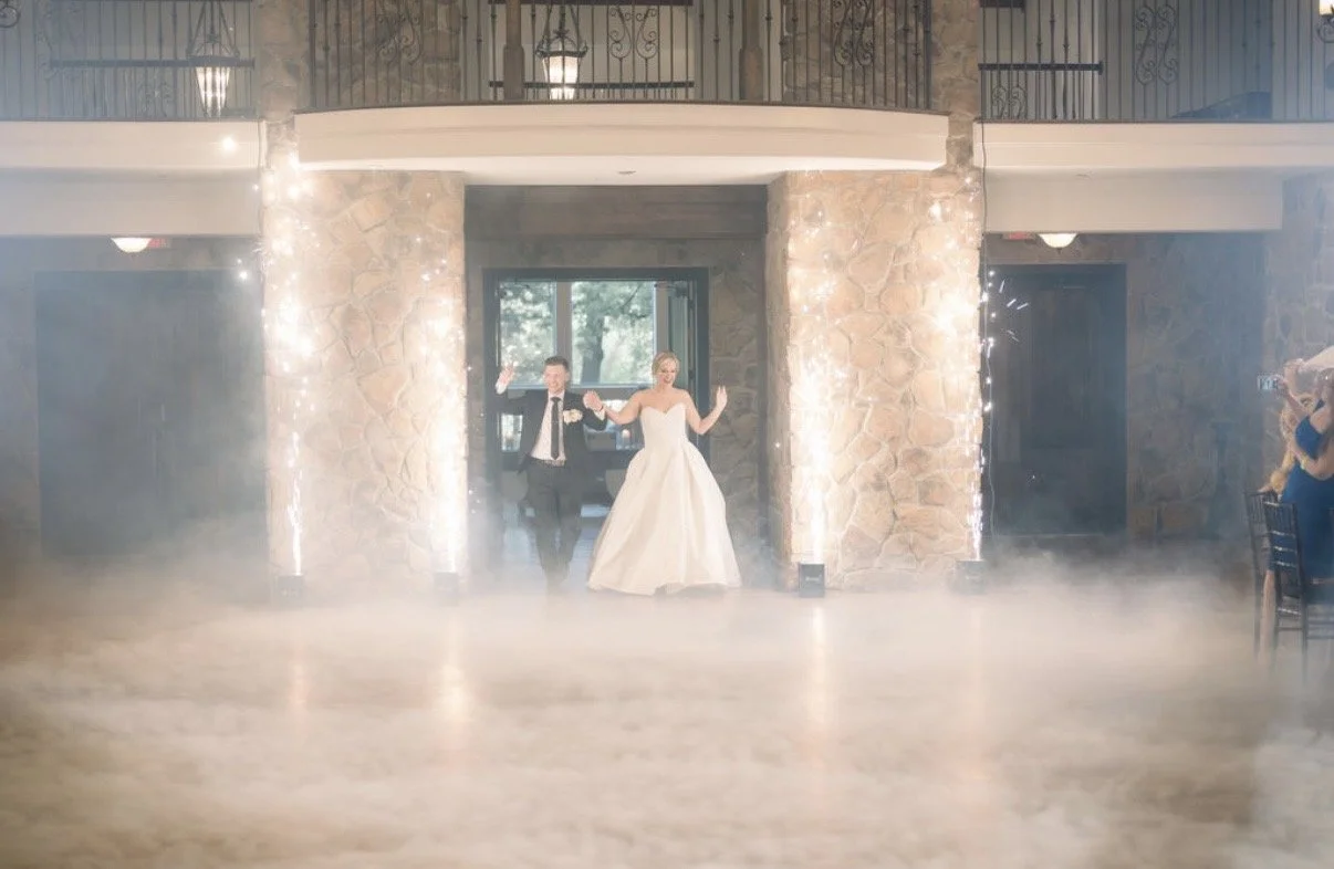 Bride and groom enter their wedding reception between cold spark fountains and low-lying fog.