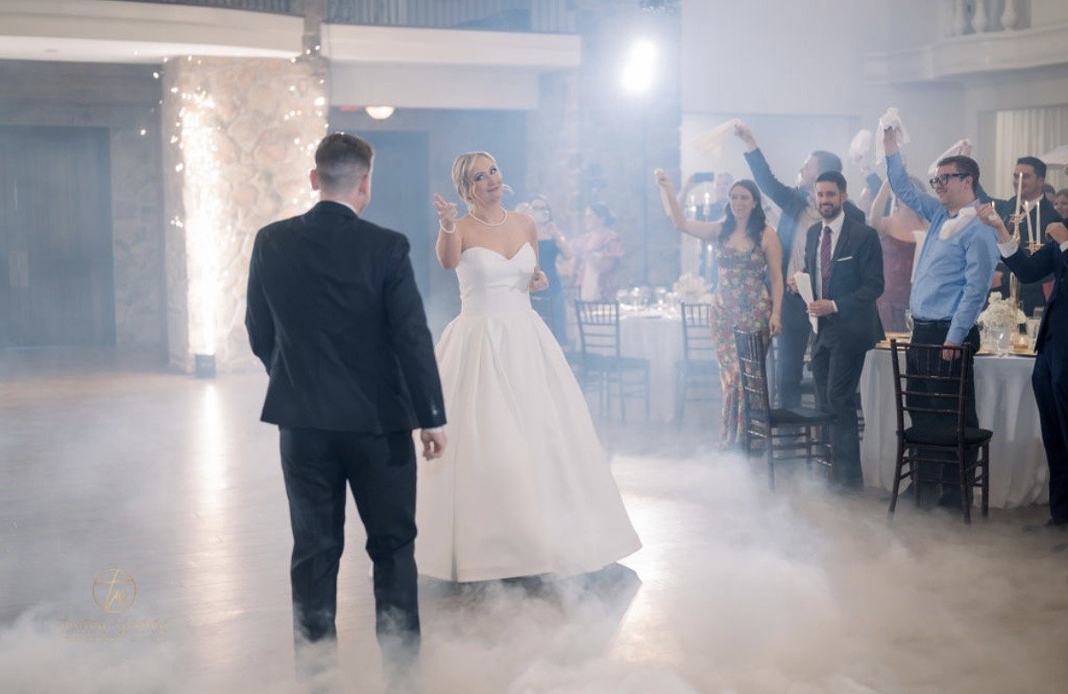 Wedding guests cheer beside cold sparks and a fog-covered dance floor.