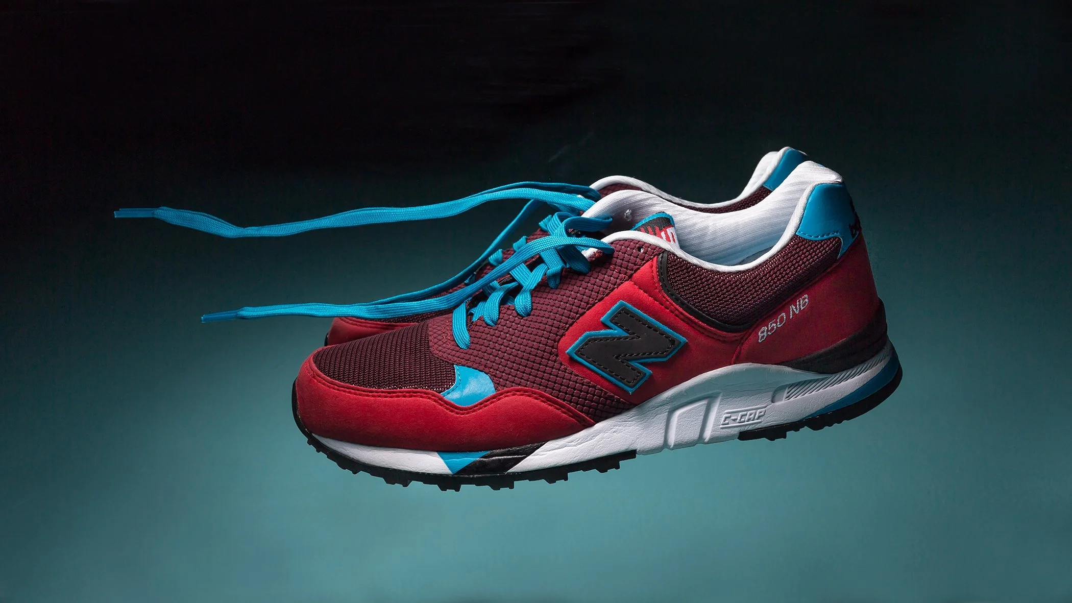 A colorful athletic sneaker with red, black, and blue accents, floating against a dark background. New Balance.