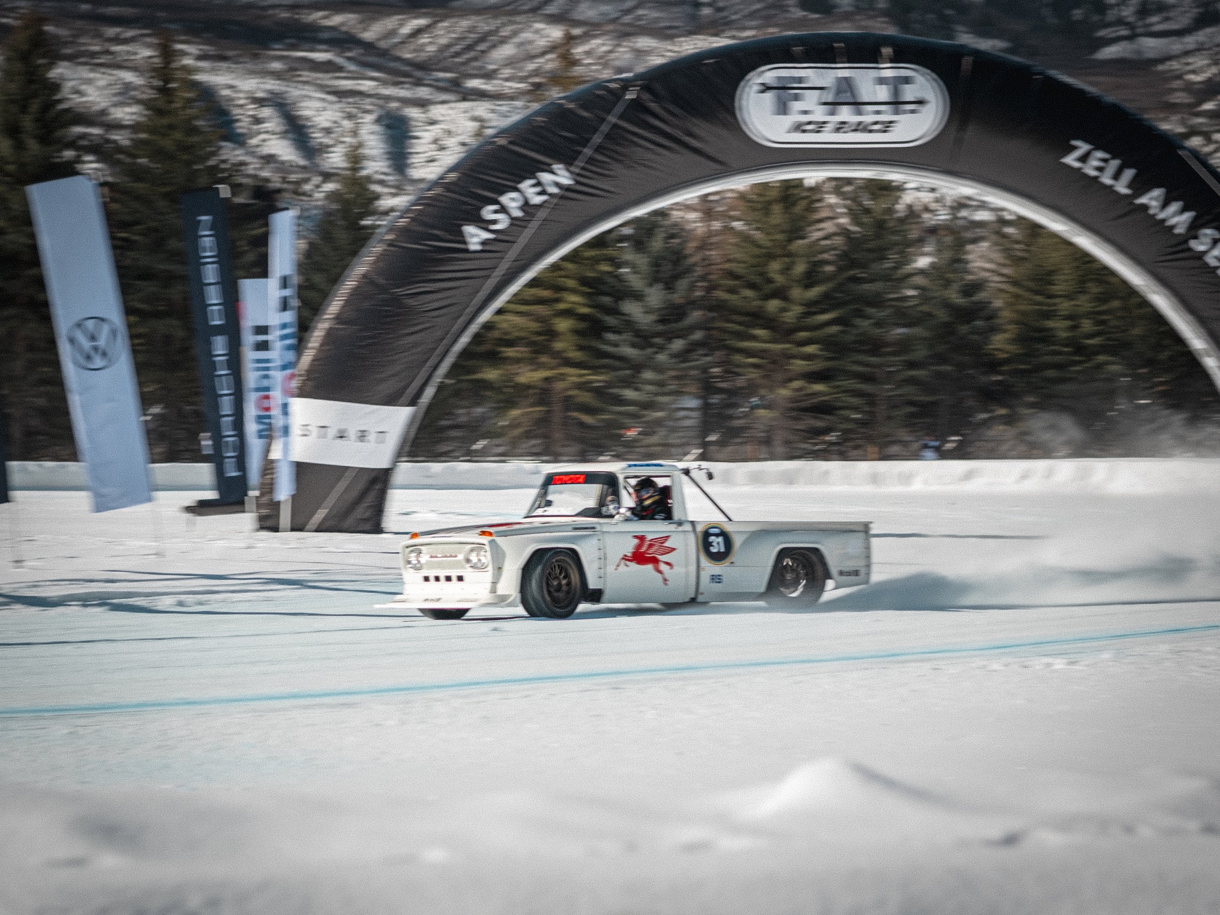 A race car on snow during a winter event, with a large tent and trees in the background. Ryan Tuerck American racing driver, Fat Ice Race, Aspen, Colorado