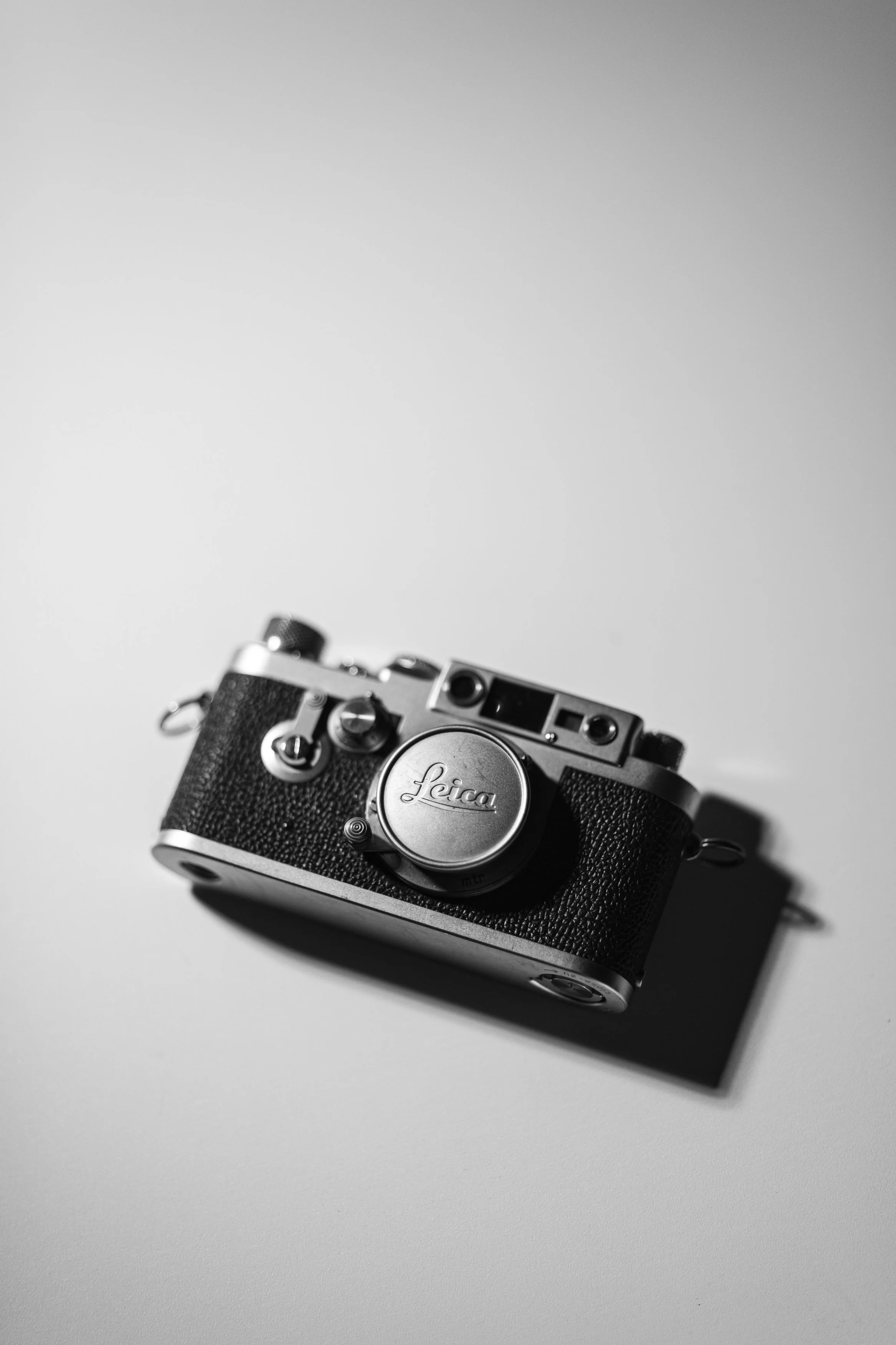 A vintage Leica camera resting on a plain surface with a neutral background.