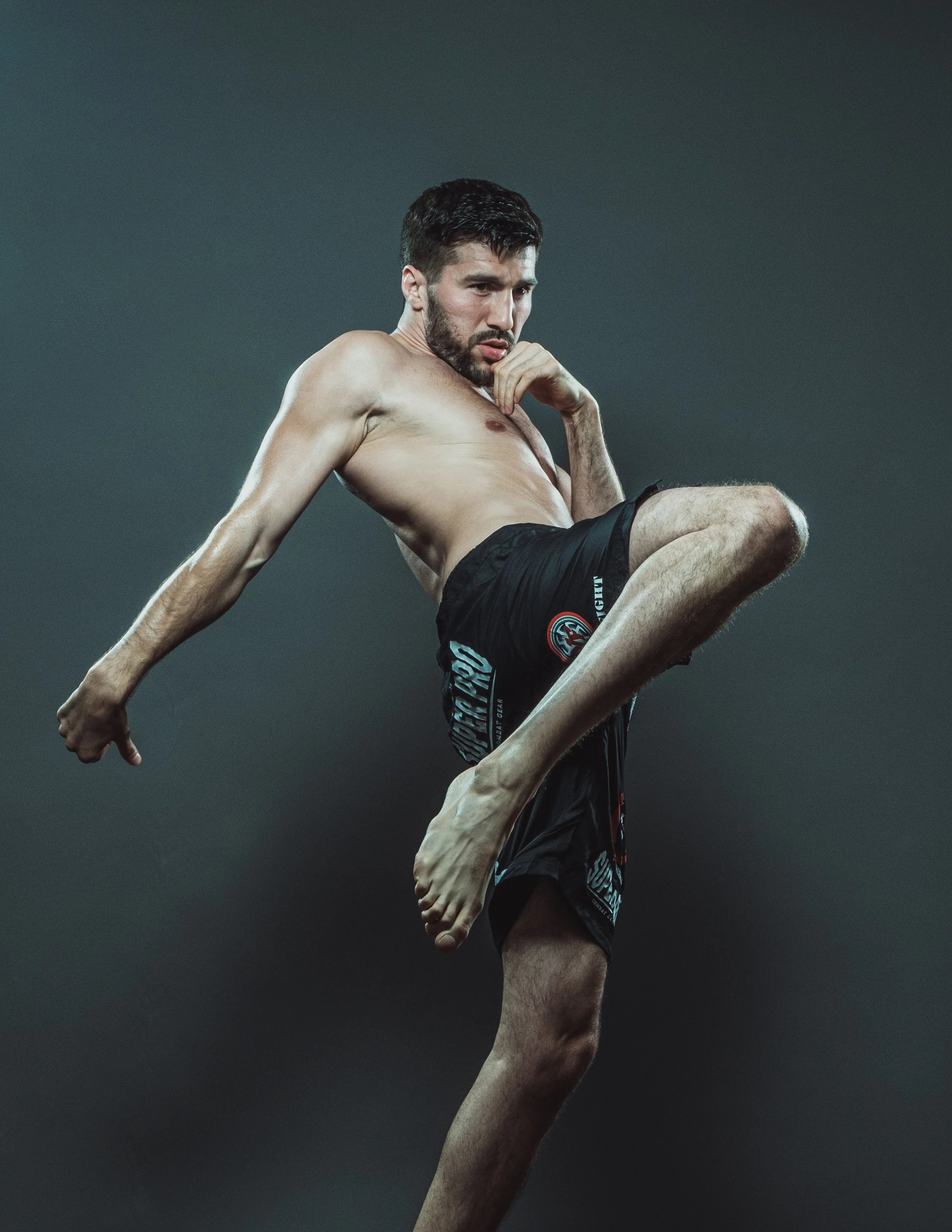 A shirtless male martial artist performing a high kick against a dark background.