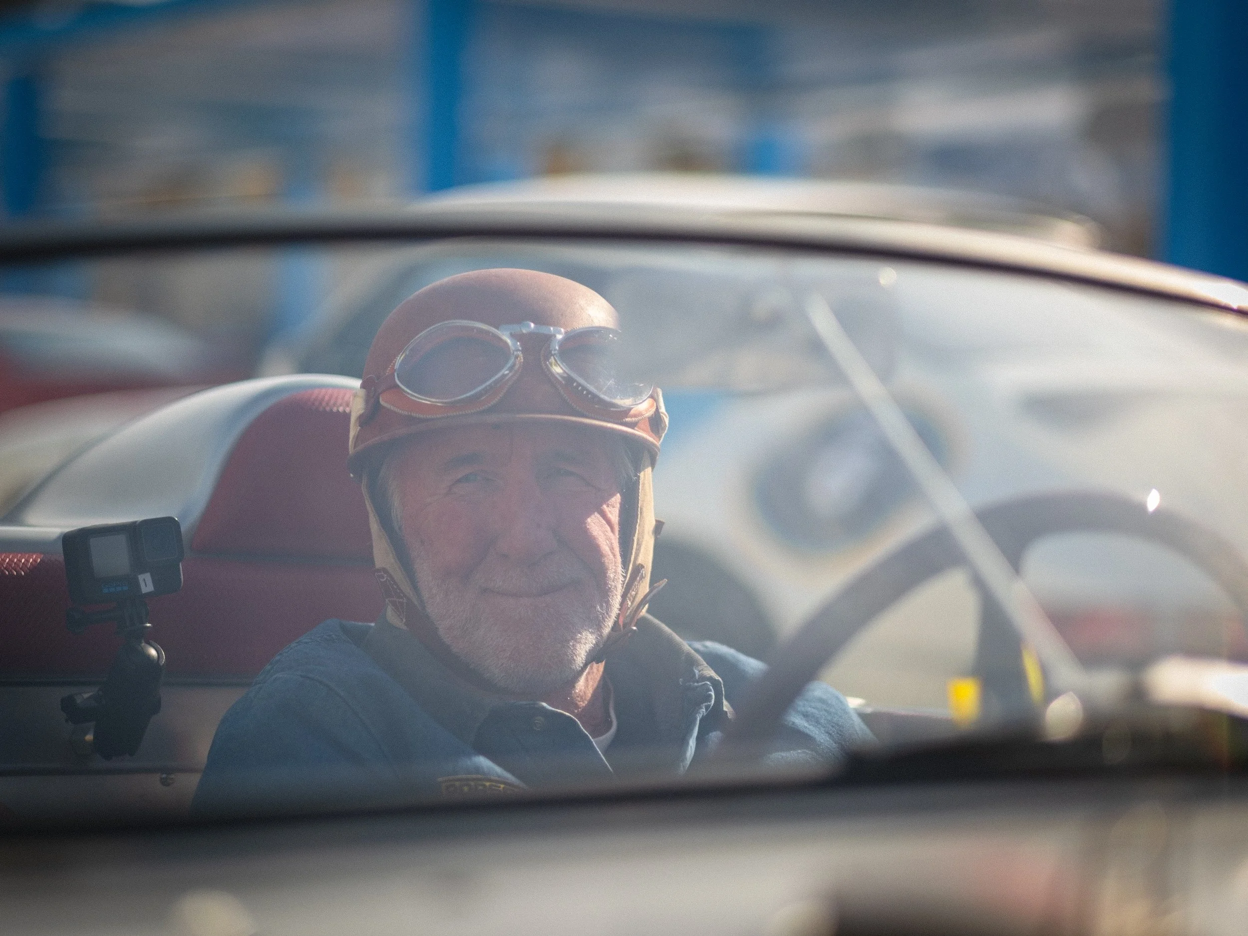 A person with a helmet and goggles sitting in a vehicle, with the photo taken from inside the vehicle showing part of the dashboard and the windshield. Jeff Zwart, Porsche, Fat Ice Race, Aspen, Colorado