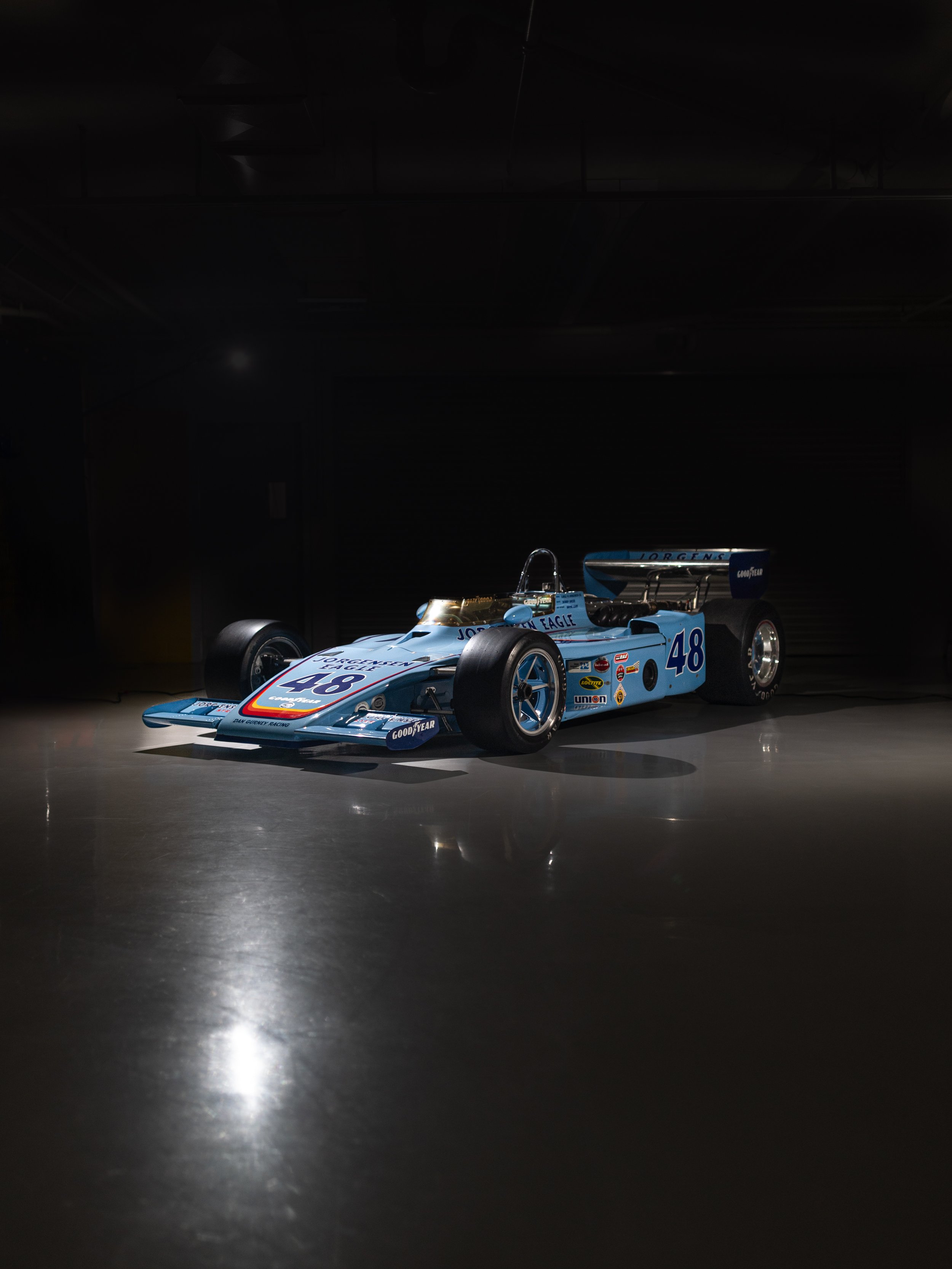 A vintage race car with the number 48 on it is illuminated against a dark background.