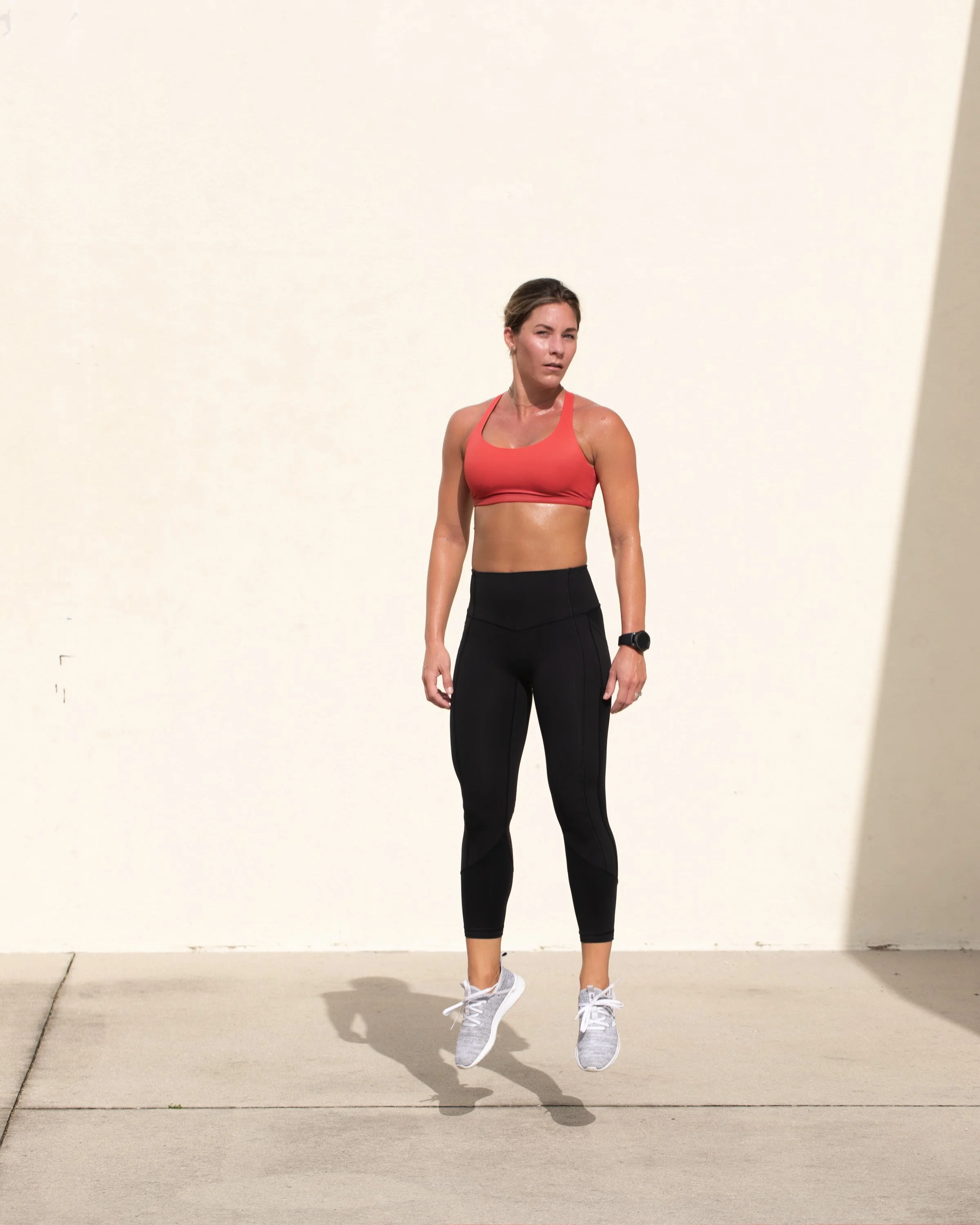 Woman in athletic outfit jumping in mid-air outdoors.