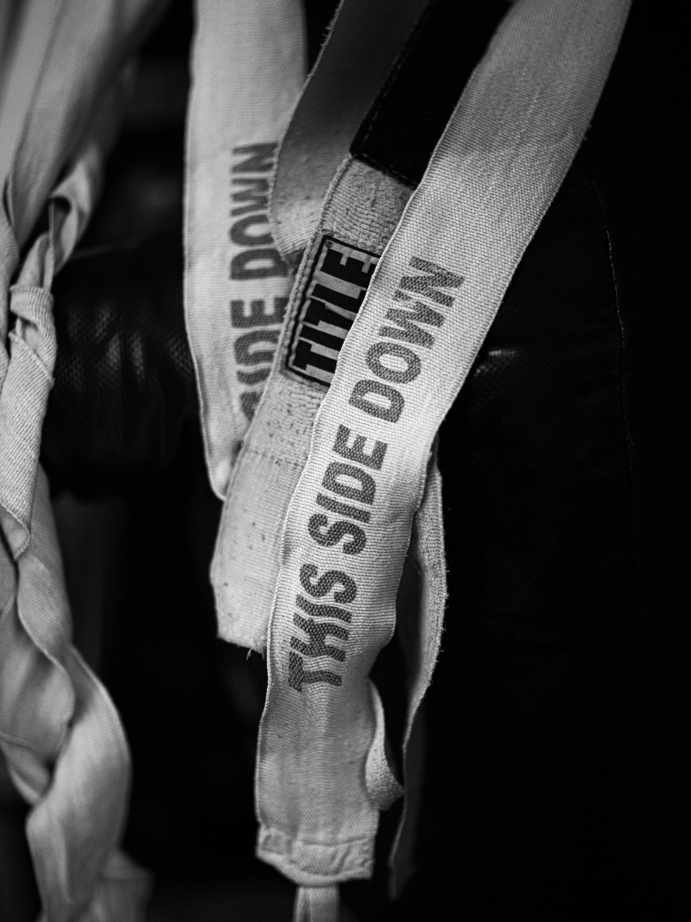 Black and white image of several fabric straps hanging vertically, with some showing text and logos. Muay Thai hand wraps