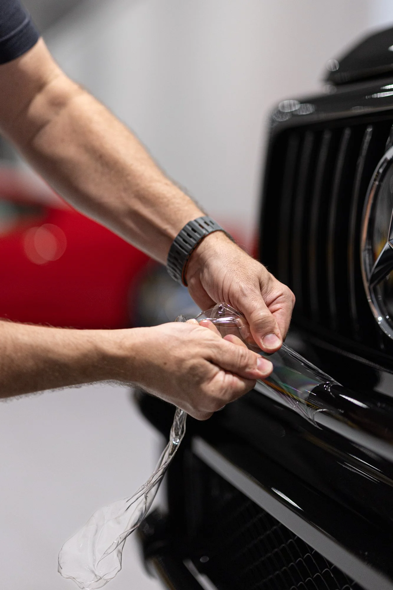 Hands applying protective clear wrap on a car's front grille.