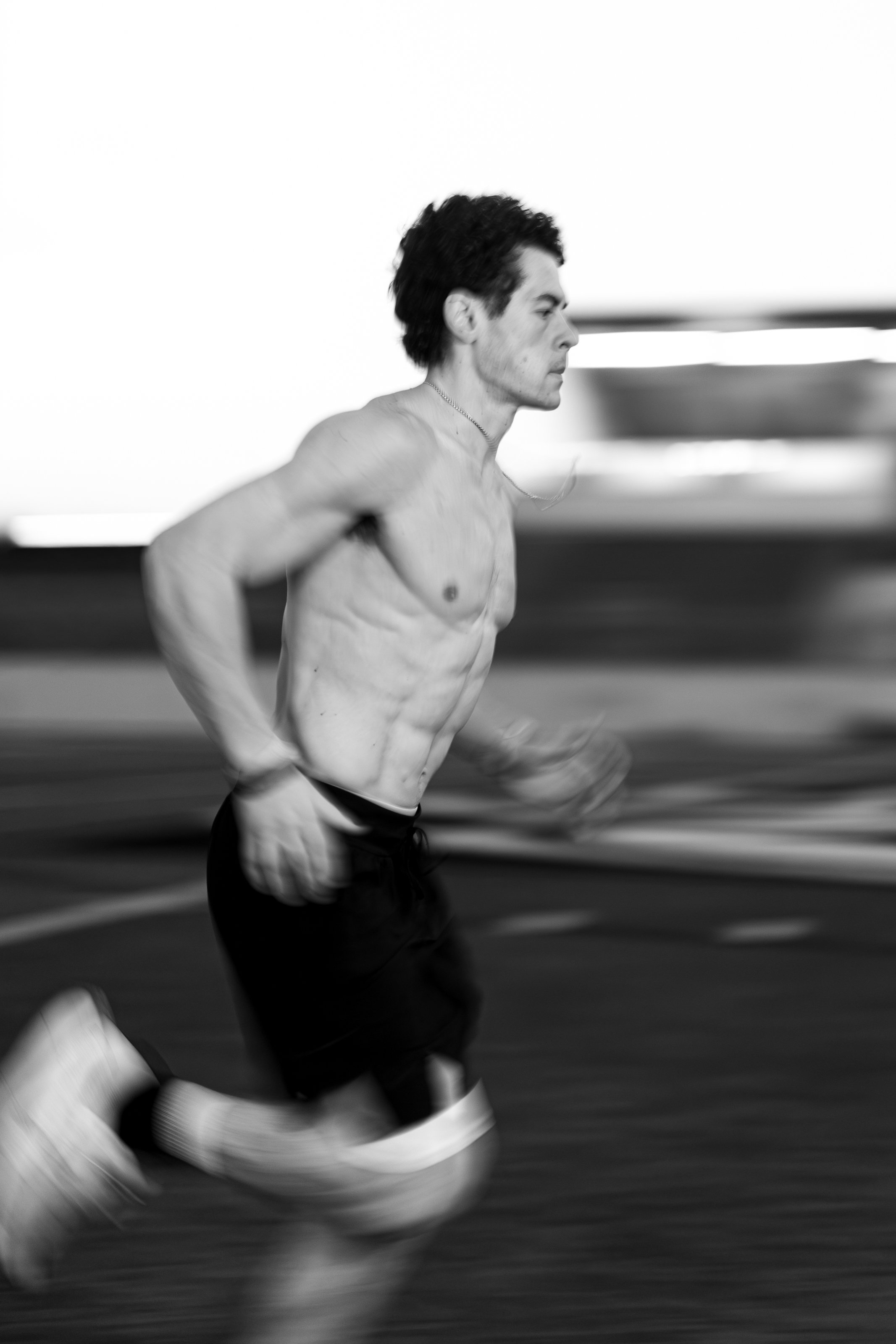 A shirtless man running in a race, with motion blur indicating speed, on a track with background movement.