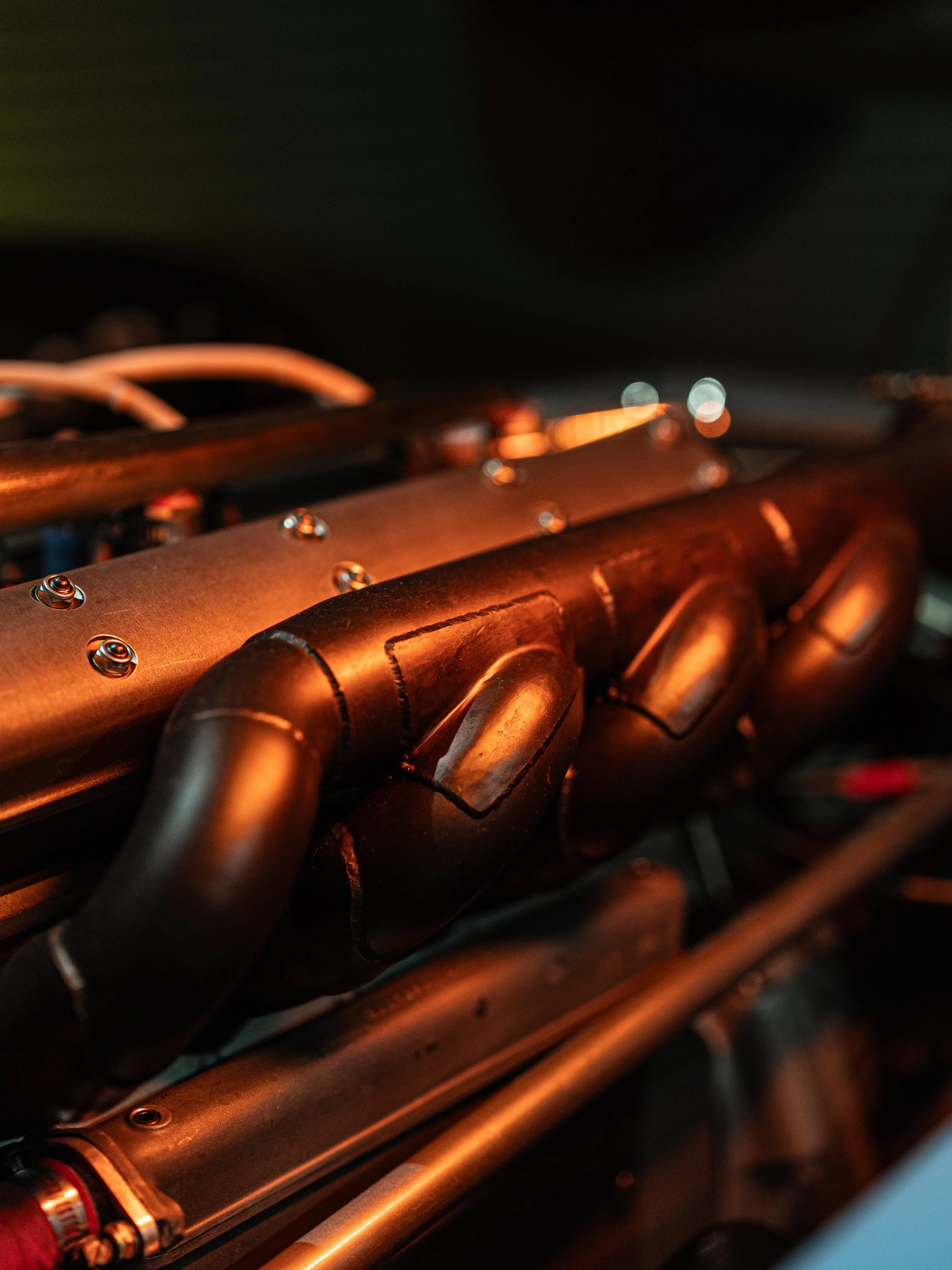 Close-up of metallic mechanical parts with screws and tubing, illuminated with warm light.
