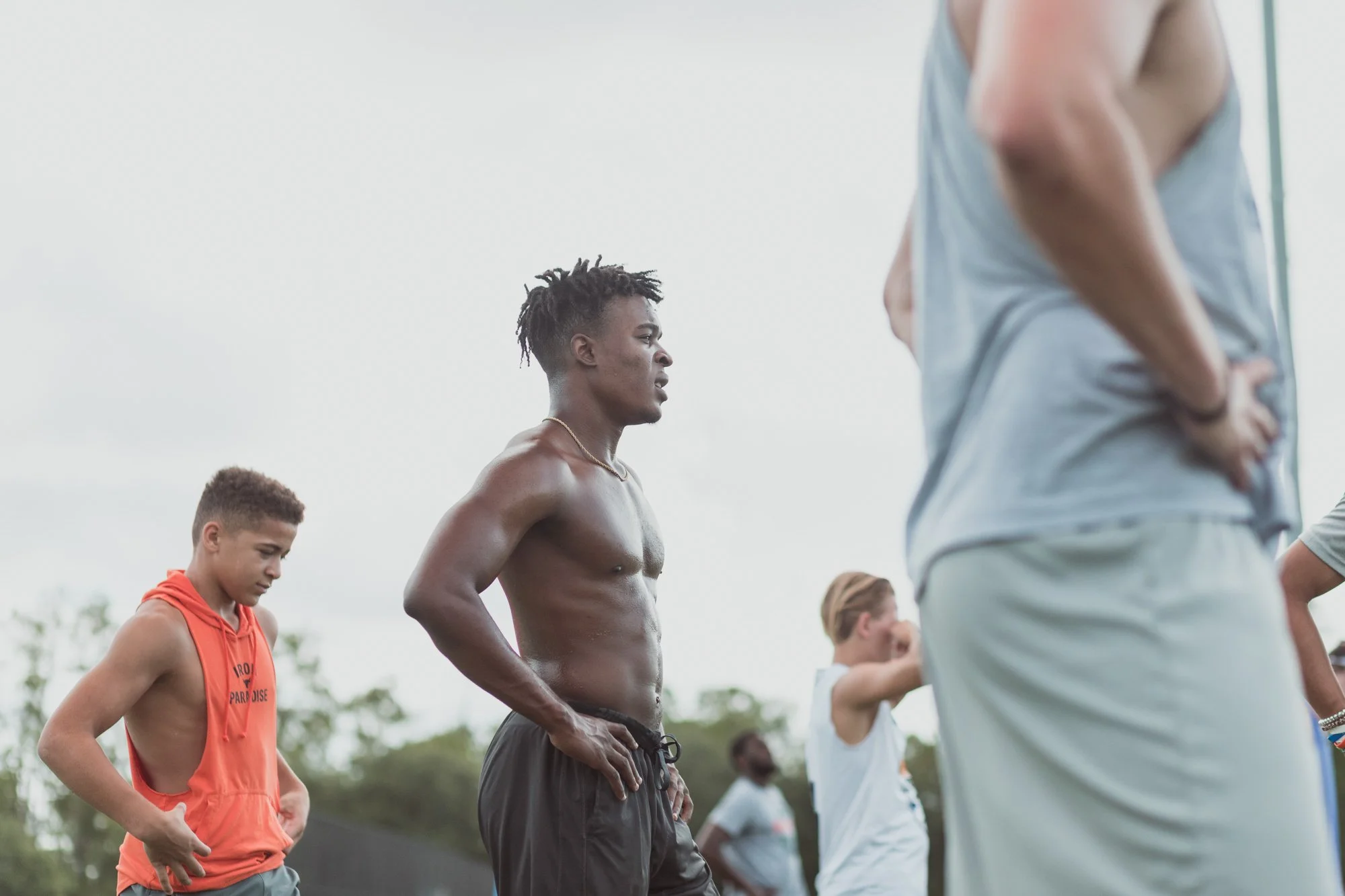 A group of young men standing outdoors, some with their hands on their hips, in a casual or athletic setting, possibly during a sports practice or event.