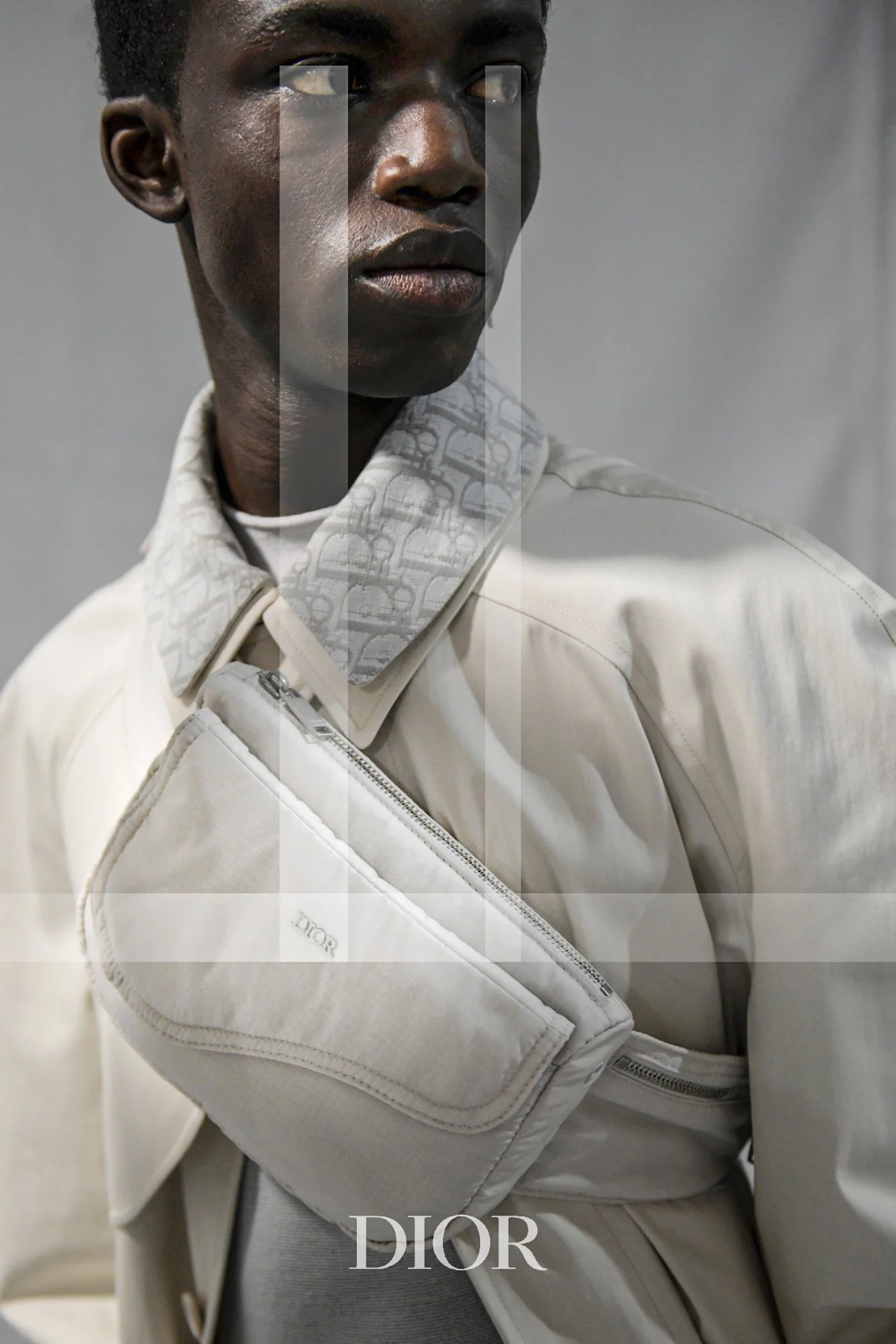 A person wearing a white Dior jacket, with a close-up focus on the face and upper body. The background is neutral gray. Christian Dior.