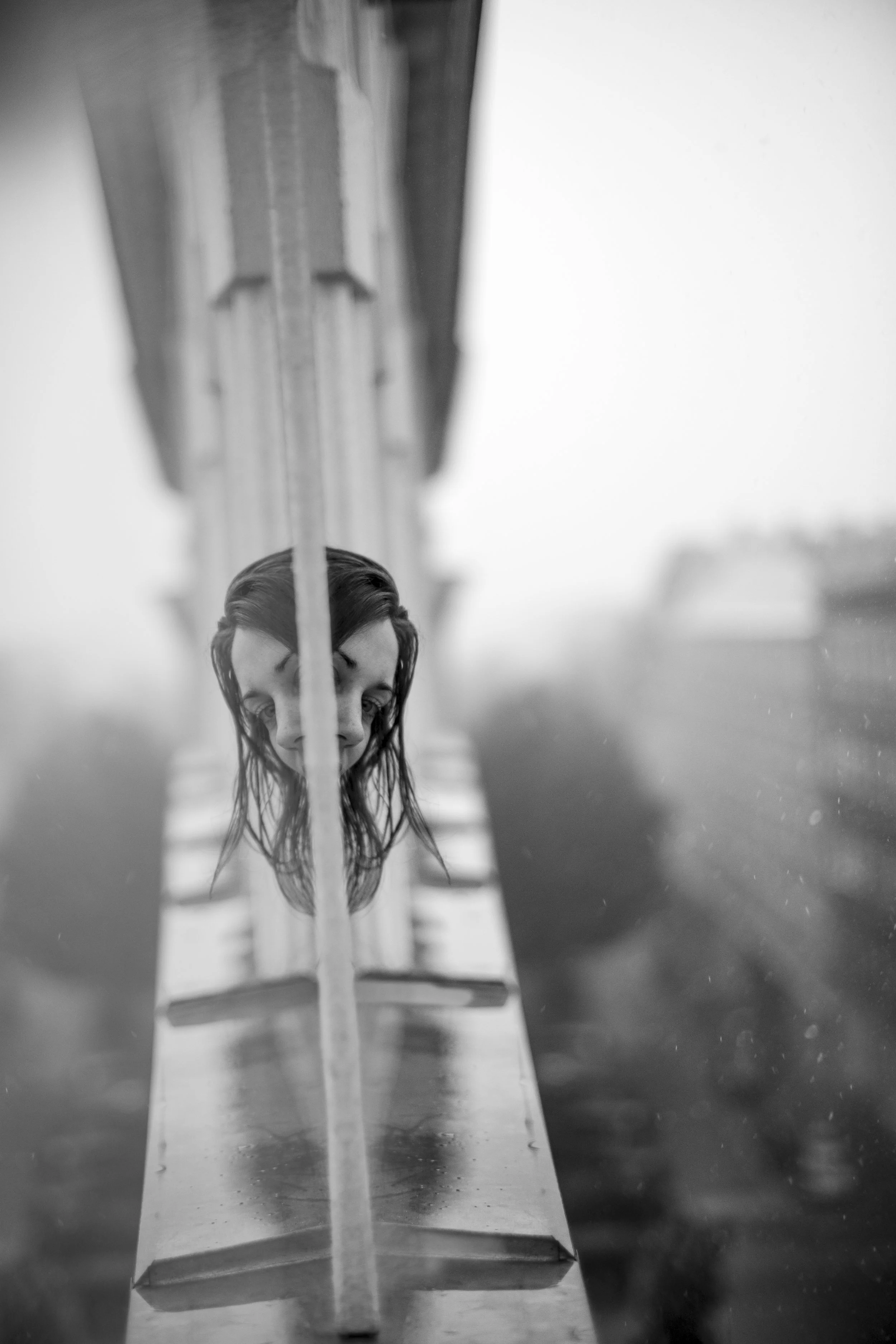 Black and white photograph of a person's face reflected in a mirror, with a blurred background.