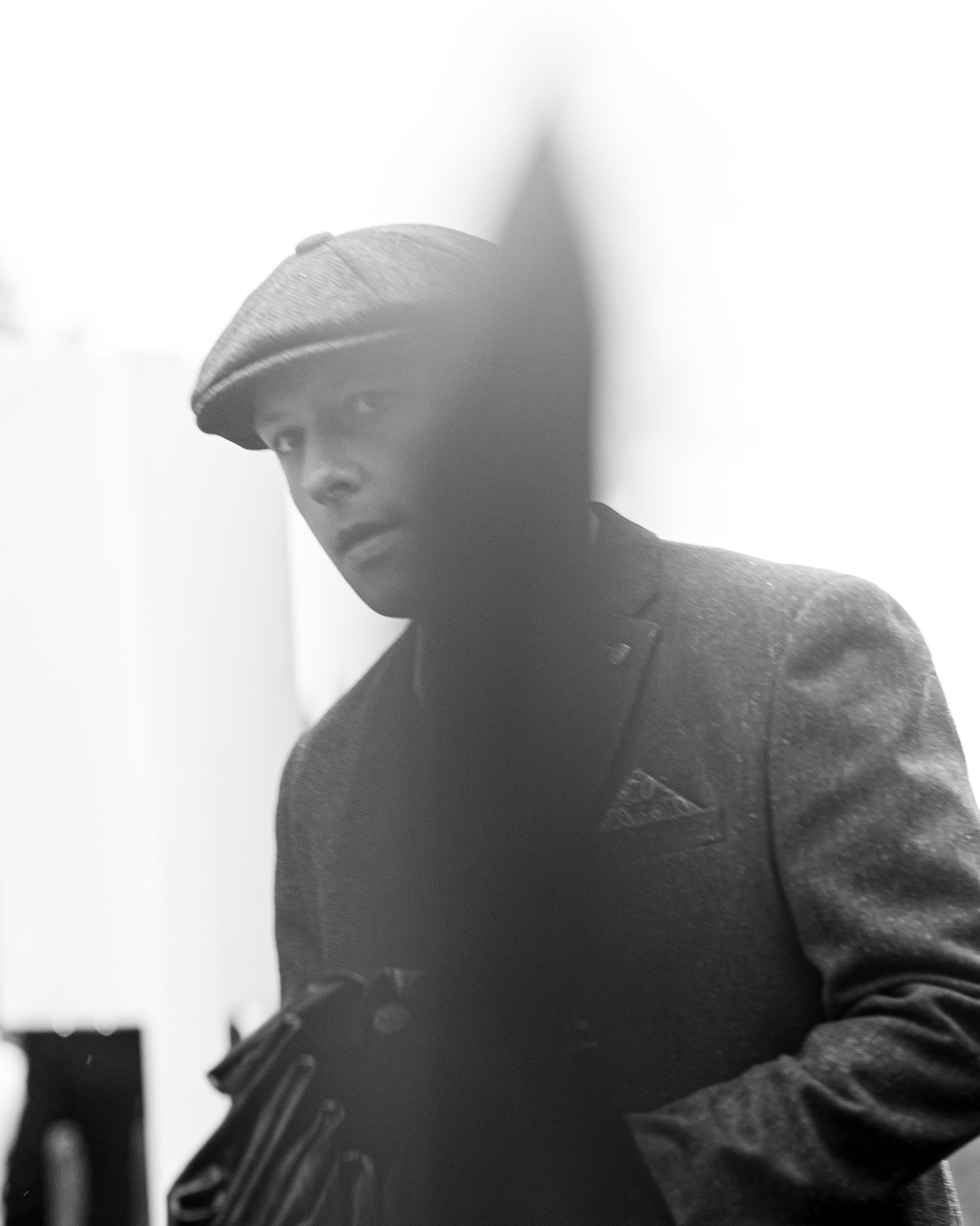 Close-up black and white photo of a person's face with a beanie, partially obscured by a shadow or object.