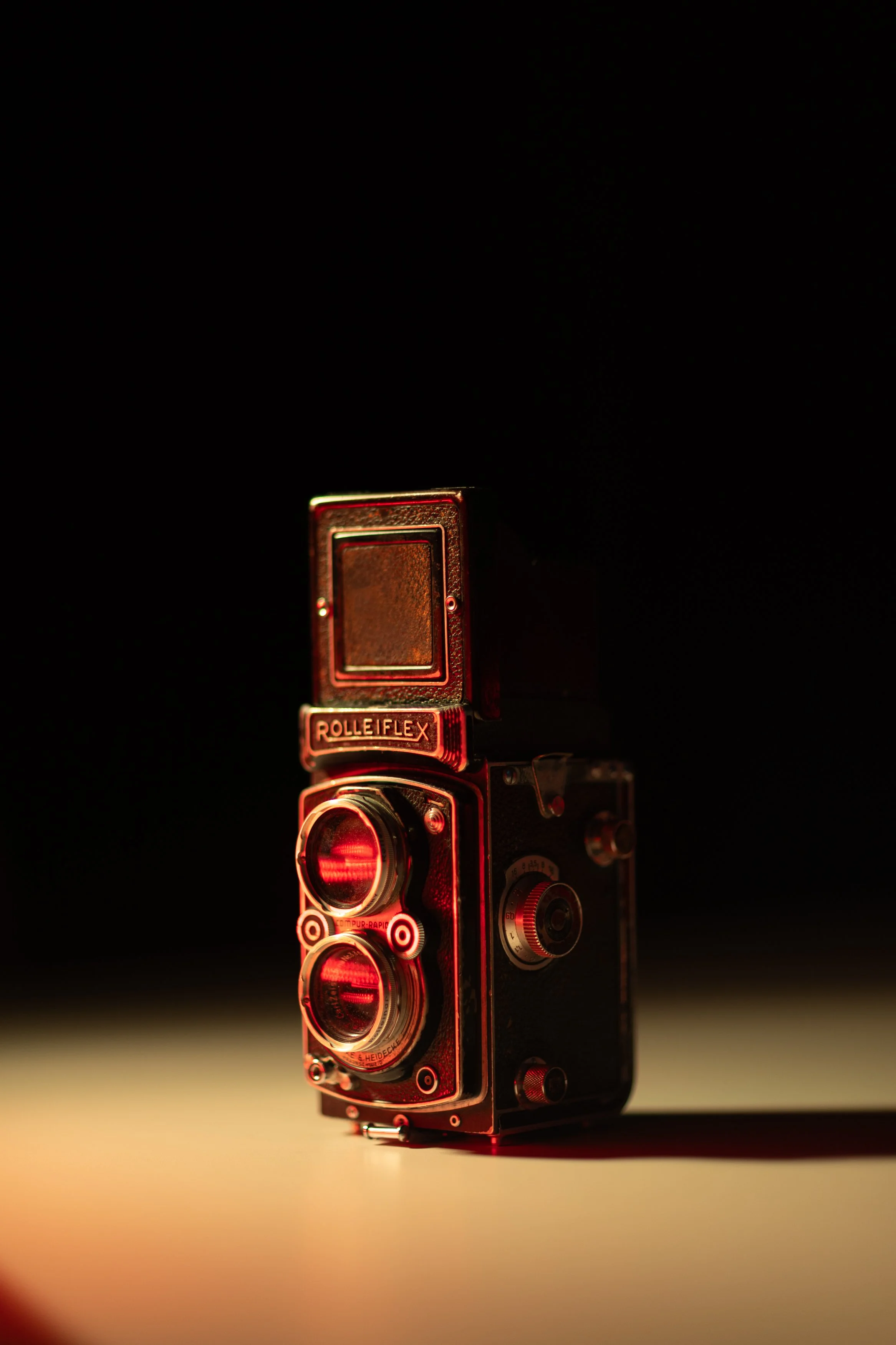 A vintage Leica camera with a red light shining from its lenses, set against a dark background and illuminated softly, creating a dramatic atmosphere.