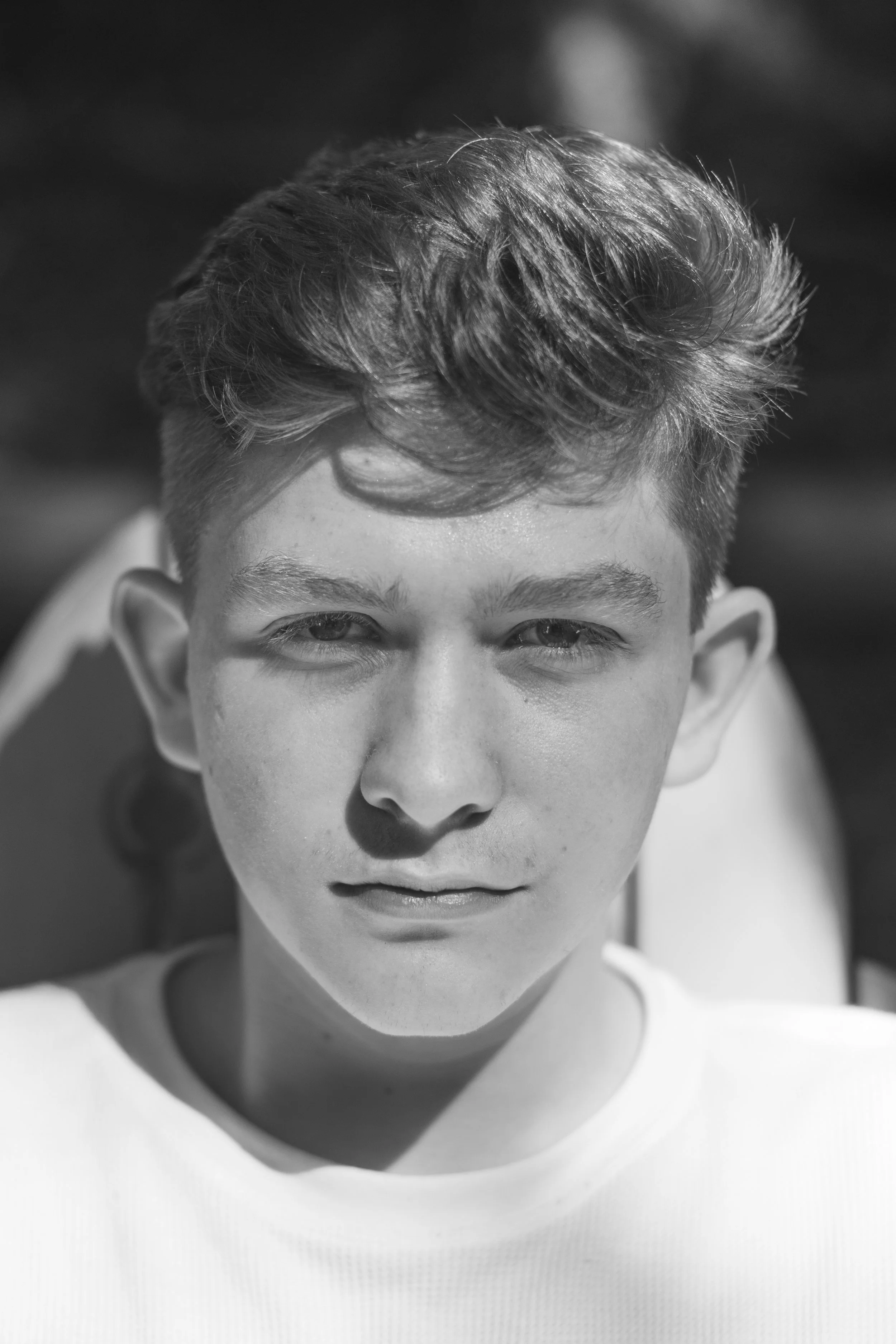 Close-up black and white portrait of a young man with styled hair, looking directly at the camera.