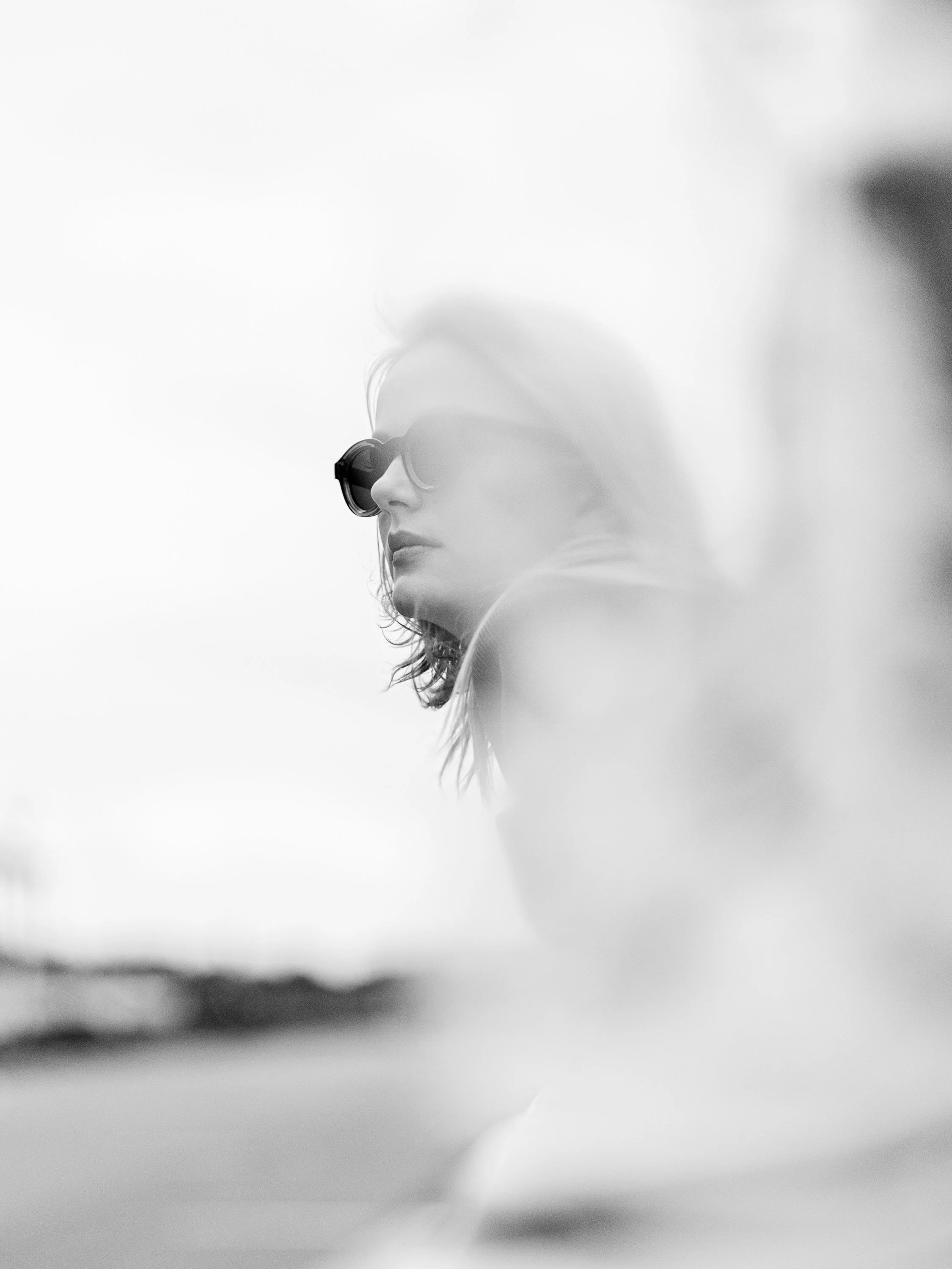 Black and white photo of a woman wearing sunglasses, viewed from the side, with her face turned away from the camera.