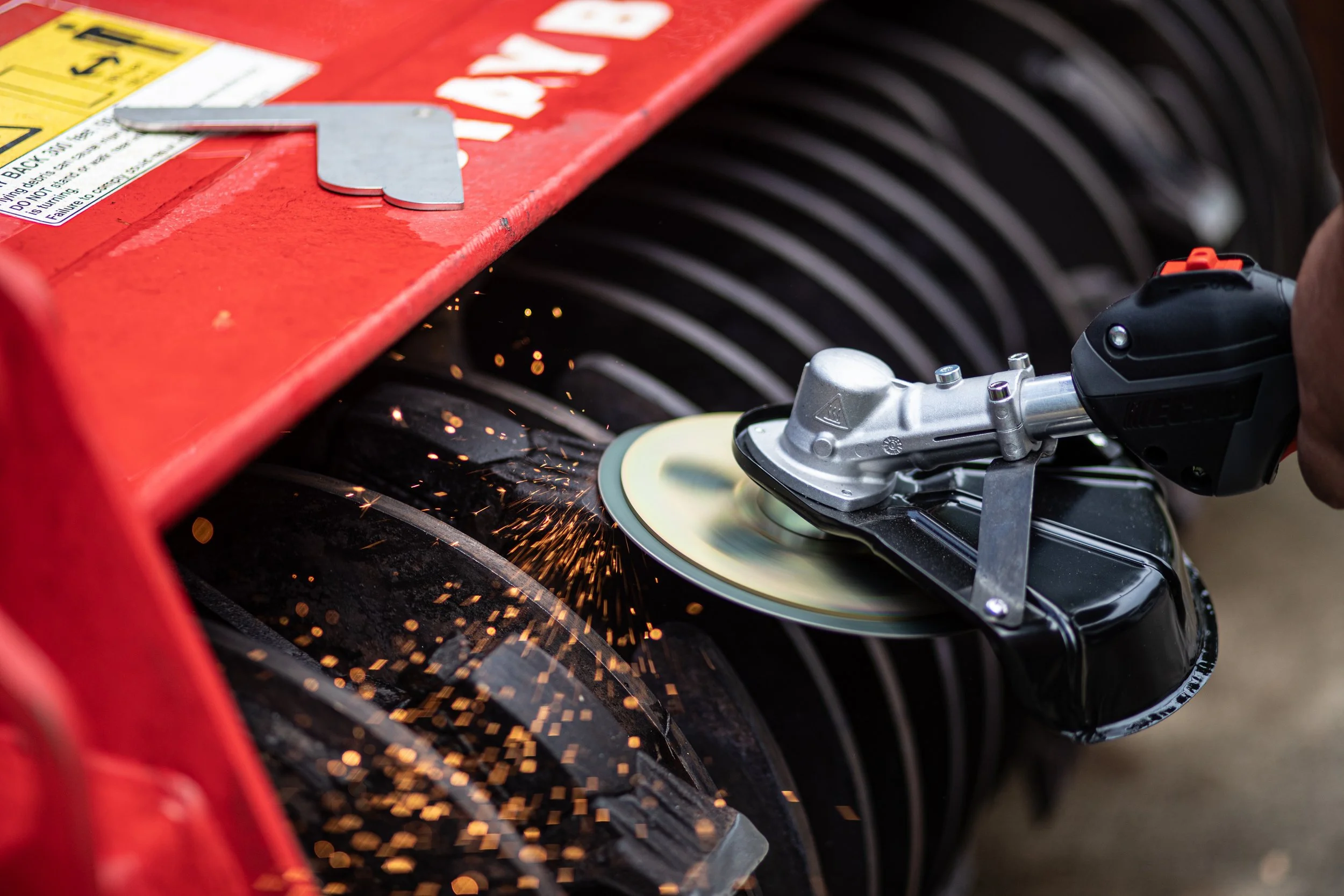 A worker using a power sander to smooth a black tire with sparks flying, on a red workbench.