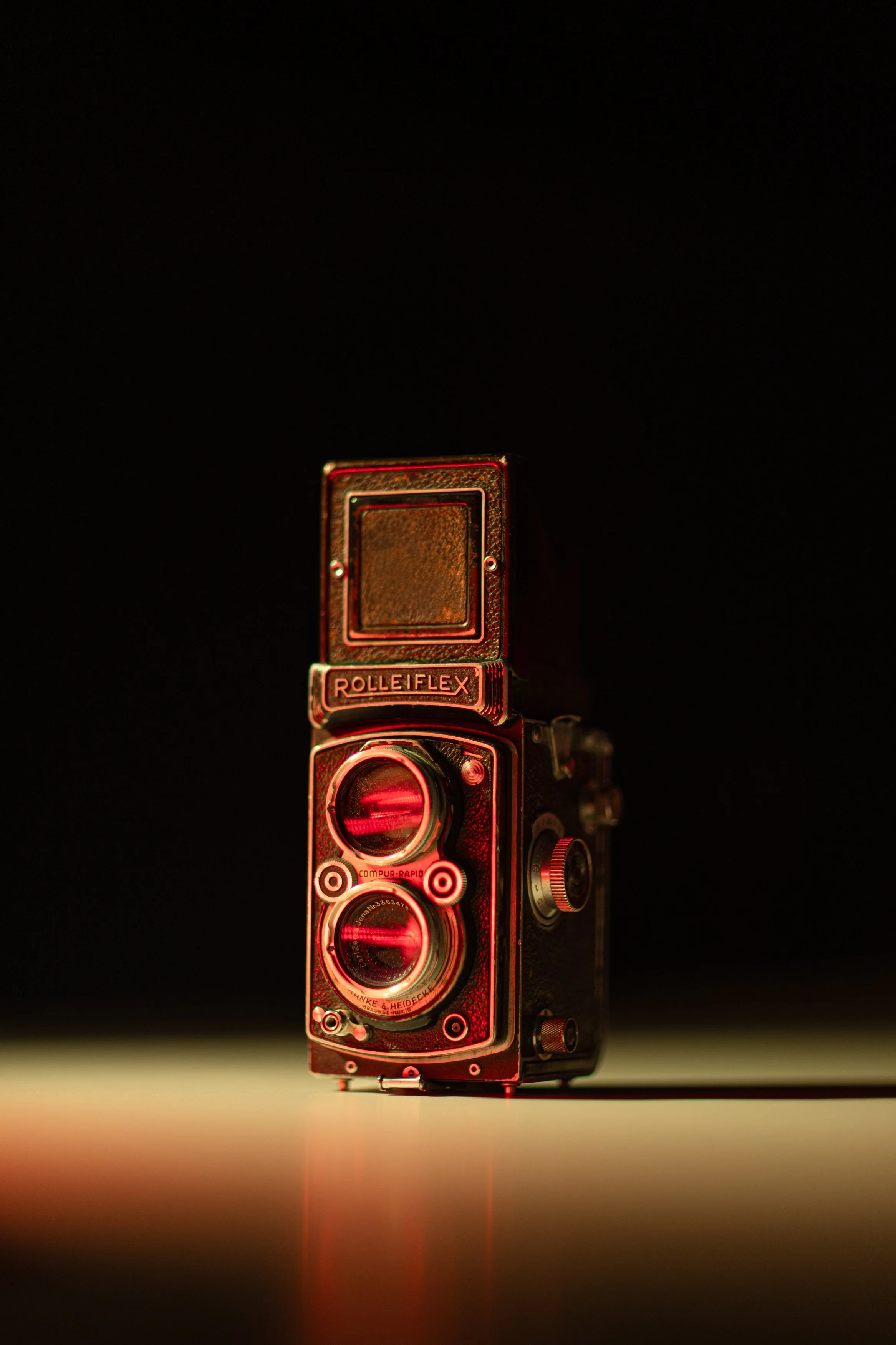 A vintage Rolleiflex twin lens reflex camera with red lighting accents on a dark background.