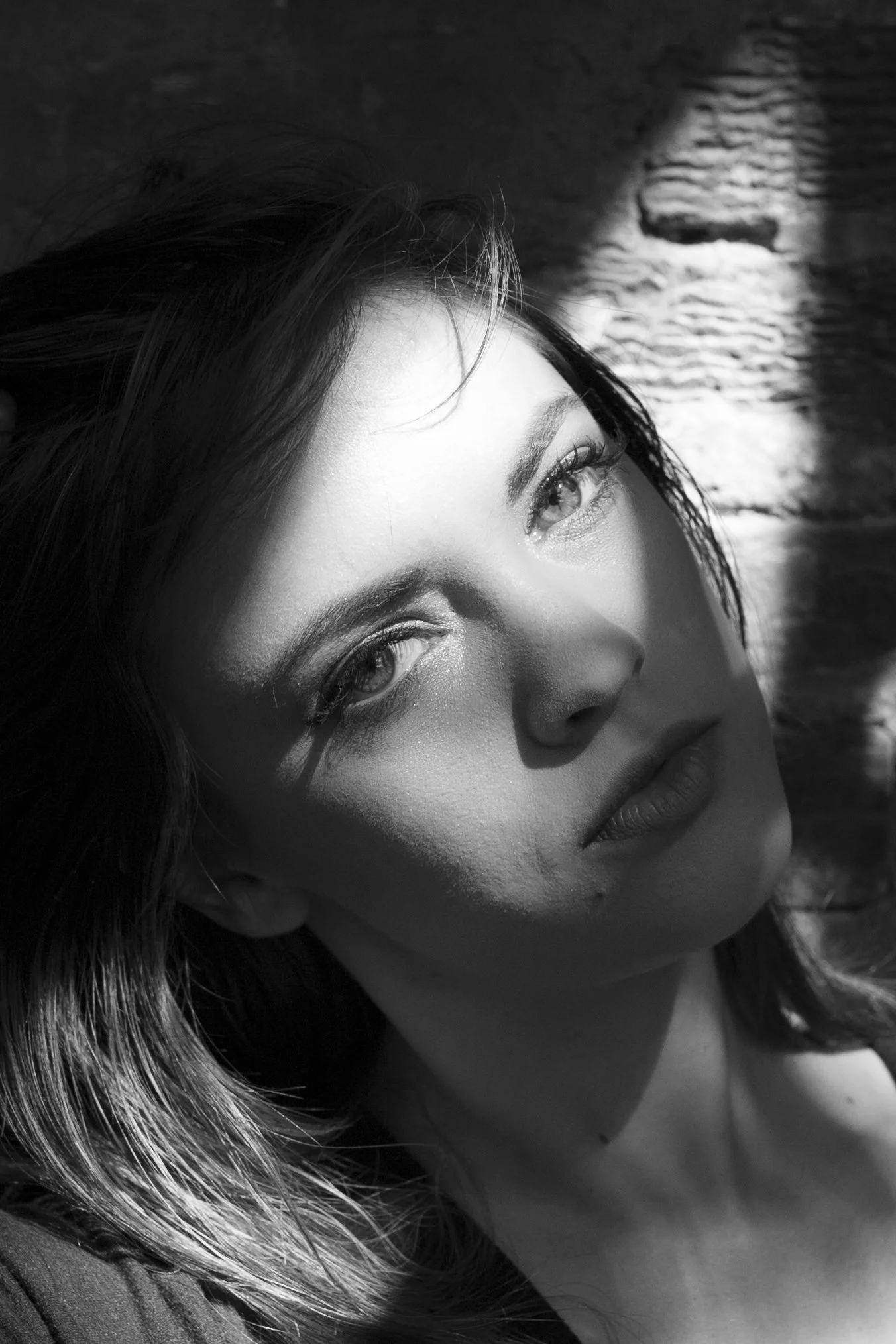 Close-up of a woman's face in black and white, with her eye and part of her mouth visible, lying on a textured surface with a light source illuminating her face and hair.