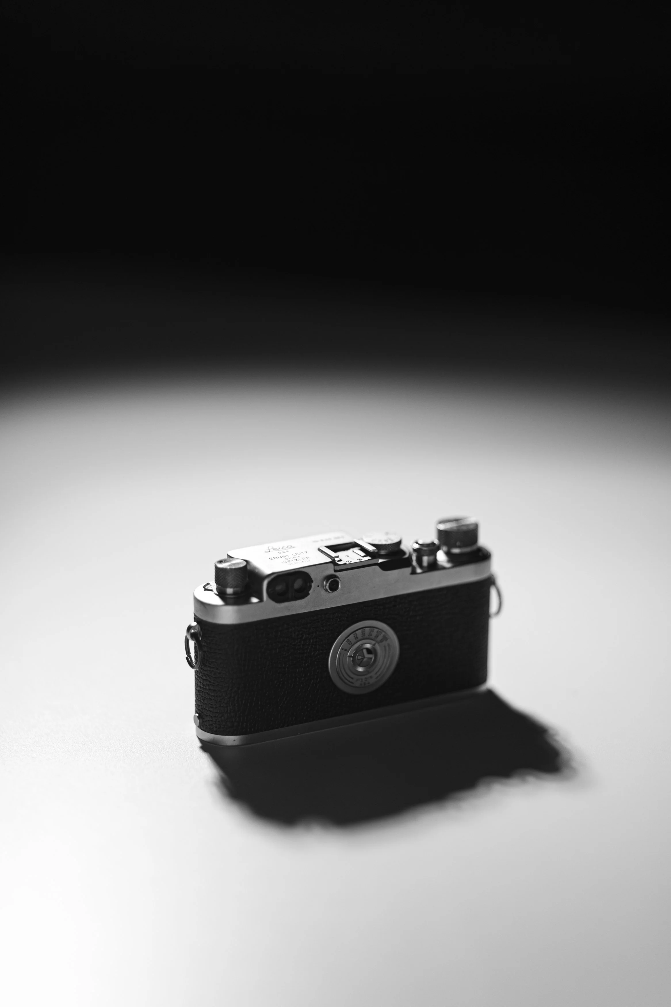 Black and white photo of a vintage camera sitting on a plain surface with a shadow cast behind it.